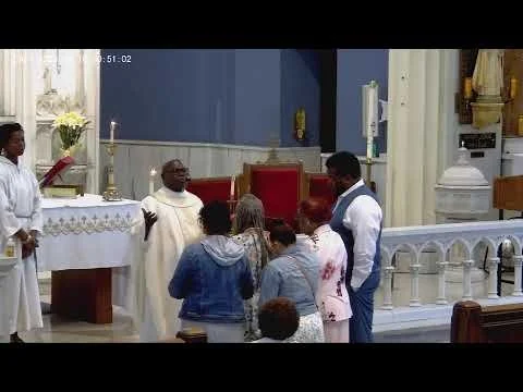 People gathered in a church during a religious service, with priests and altar in the background.