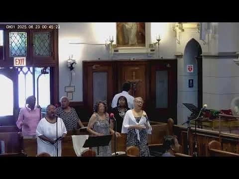 Group of people singing choir inside a church with wooden pews and religious decorations.