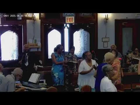 People standing and sitting inside a church, some with musical instruments, engaged in a religious service or gathering.