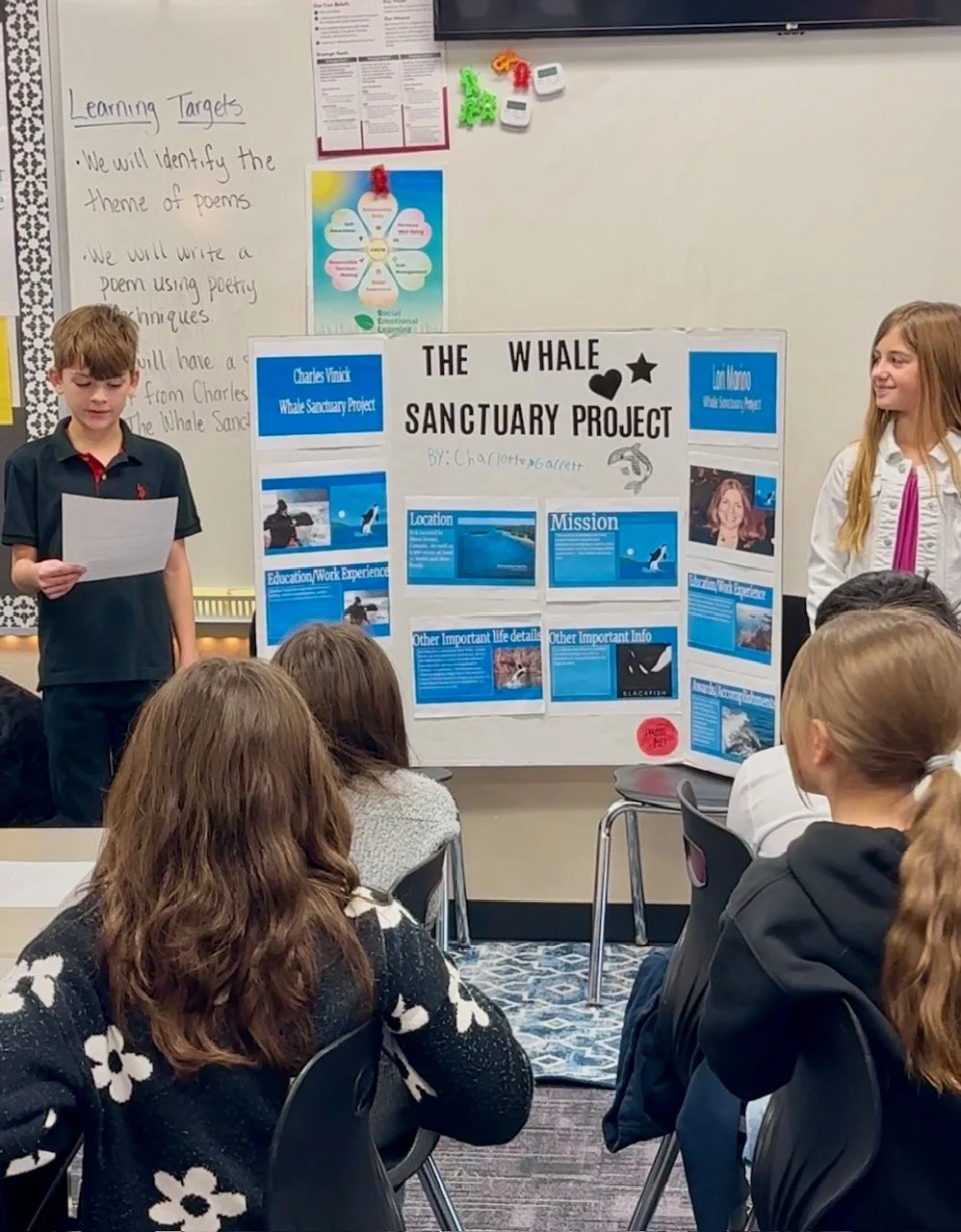 Students presenting a poster titled 'The Whale Sanctuary Project' in front of an audience in a classroom.