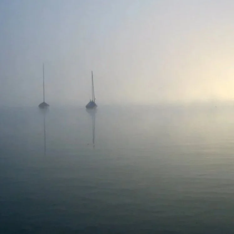 Zwei Boote auf ruhigem Wasser bei nebligem Himmel