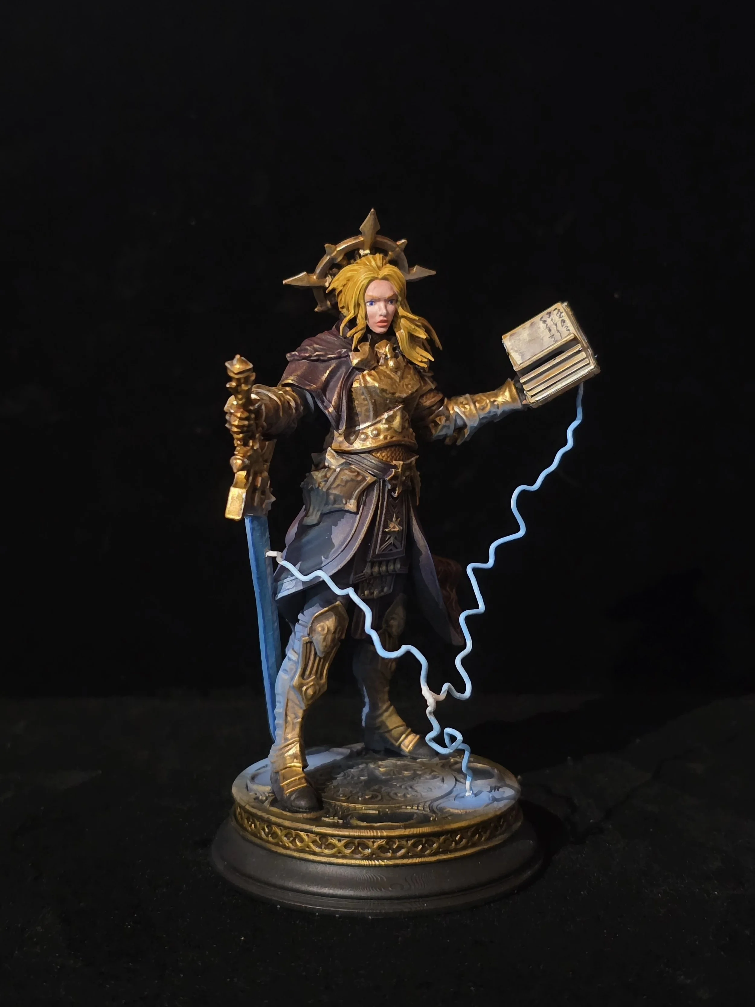 A detailed miniature figurine of a female warrior holding a sword in one hand and a lightning bolt-conducting book in the other, standing on a decorated base with a dark background.