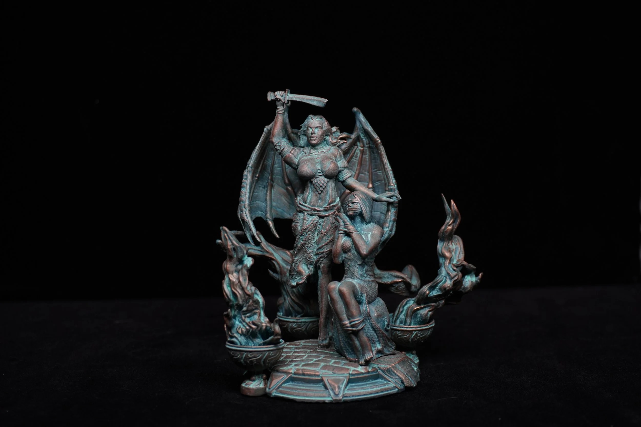 A detailed sculpture of a female warrior with wings, holding a sword above her head, standing on a base with a kneeling woman and flames.