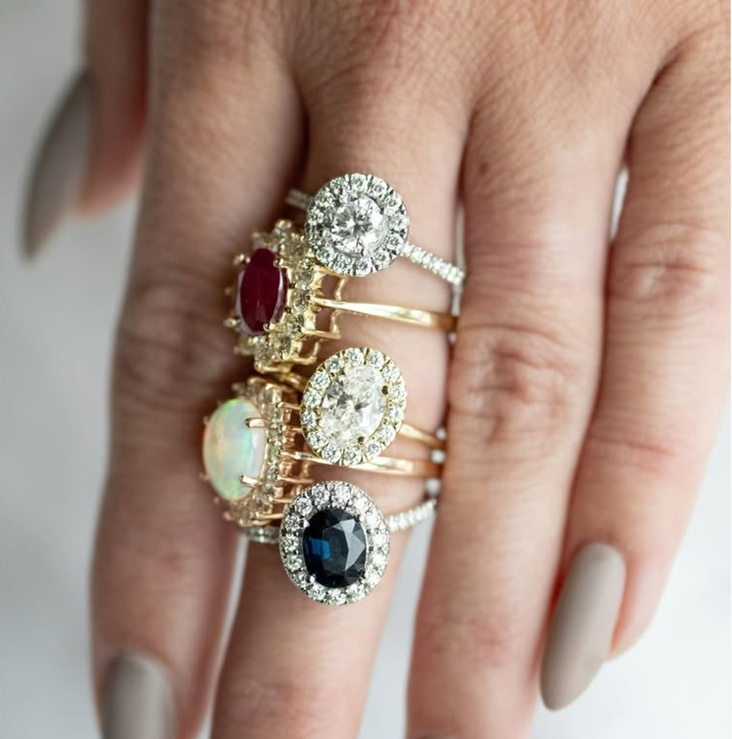 Hand wearing multiple gold rings with large oval-shaped, halo, and gemstone designs.