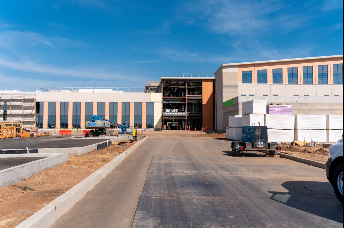Under construction building with construction equipment, materials, and workers on site under a blue sky.