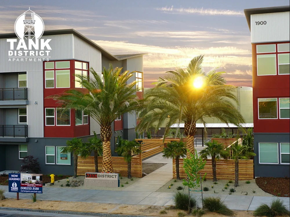 Modern multi-story apartment complex with palm trees and sunset sky, advertising Tank District Apartments.