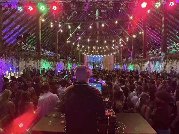 DJ performing at a crowded indoor party with string lights and floral decorations.