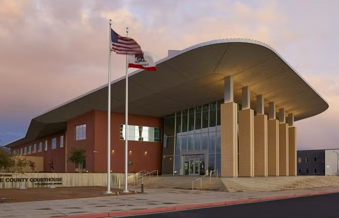 Exterior of a modern courthouse building with flags of the United States and California on flagpoles in front.