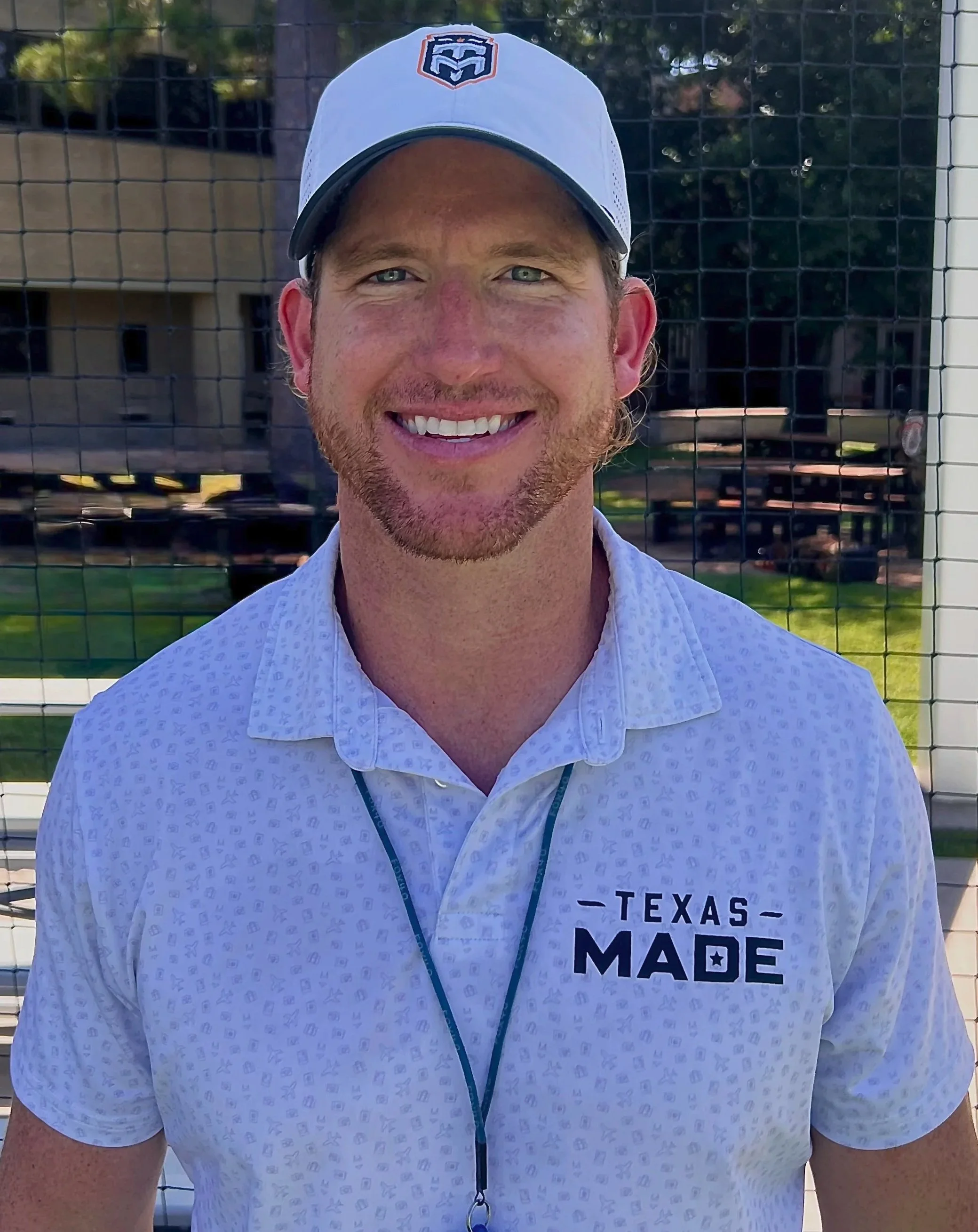 Kevin Finn smiling in a white Texas Made lacrosse polo and hat beside the field.