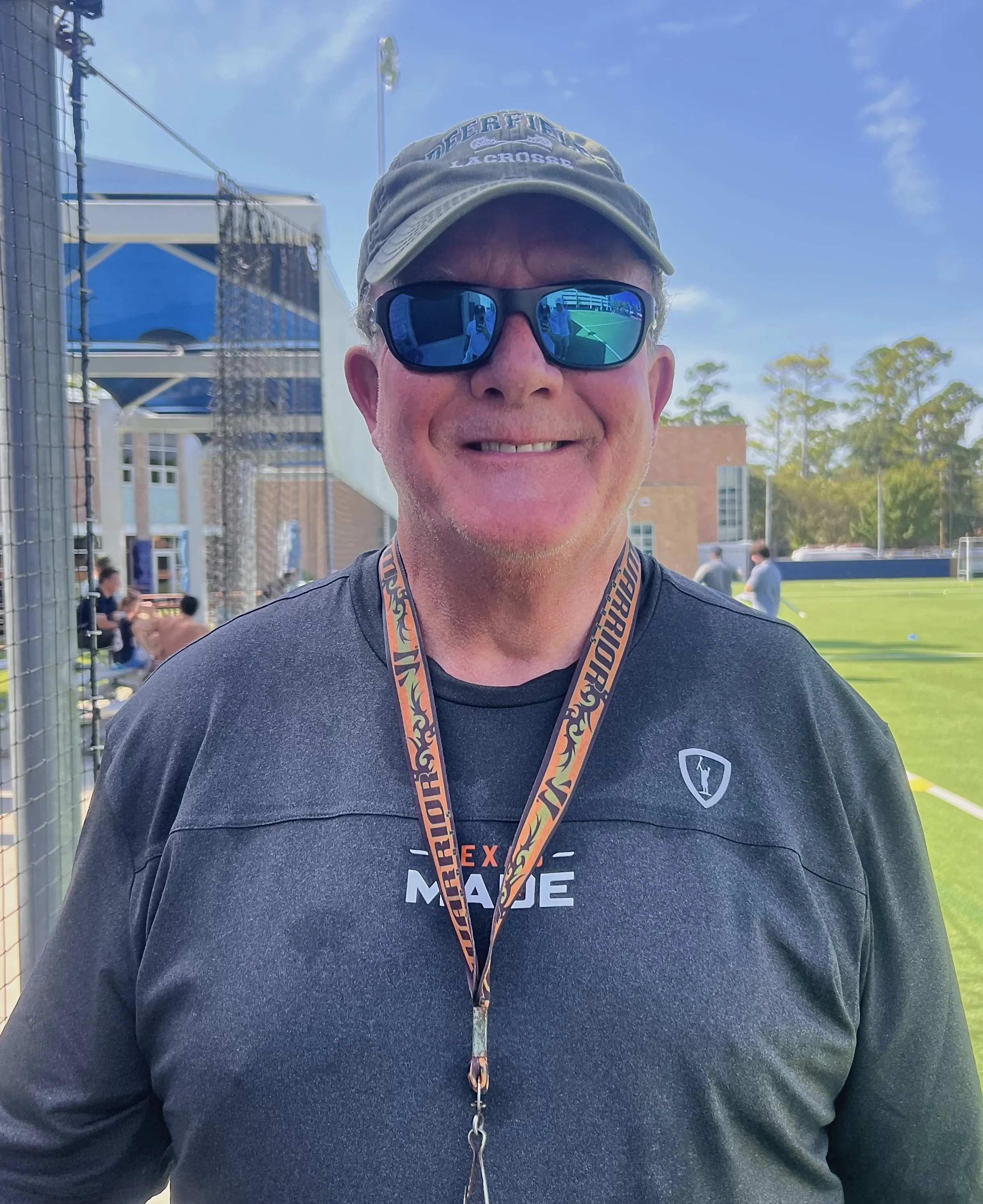 John Perouty wearing Texas Made lacrosse apparel and sunglasses beside a lacrosse field.