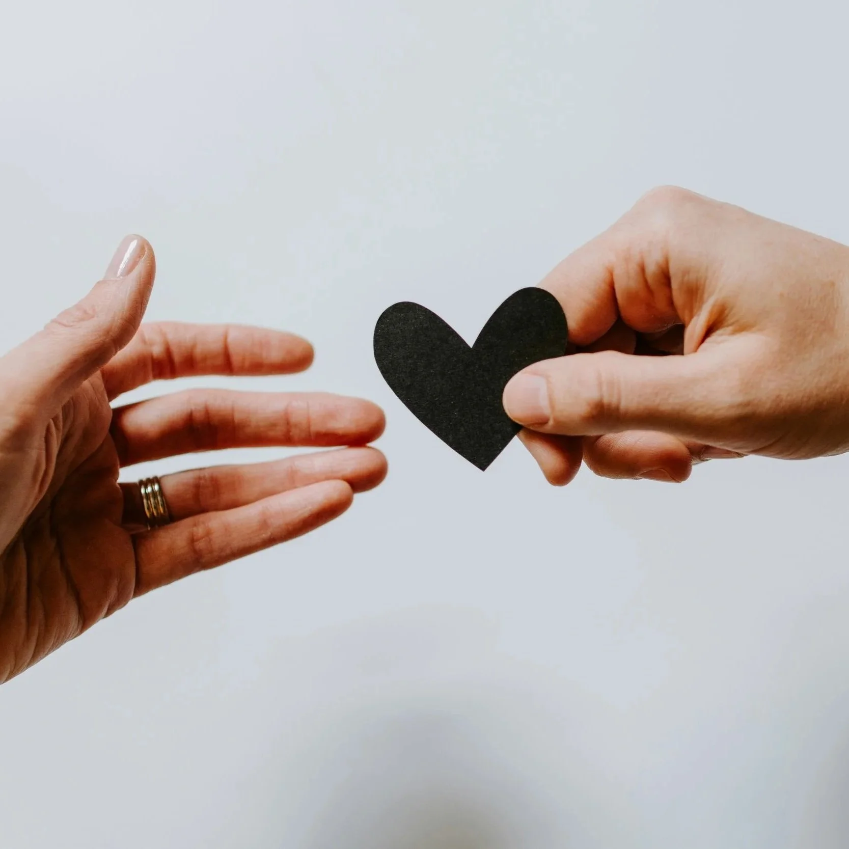 Two hands holding a black paper heart against a plain light background.