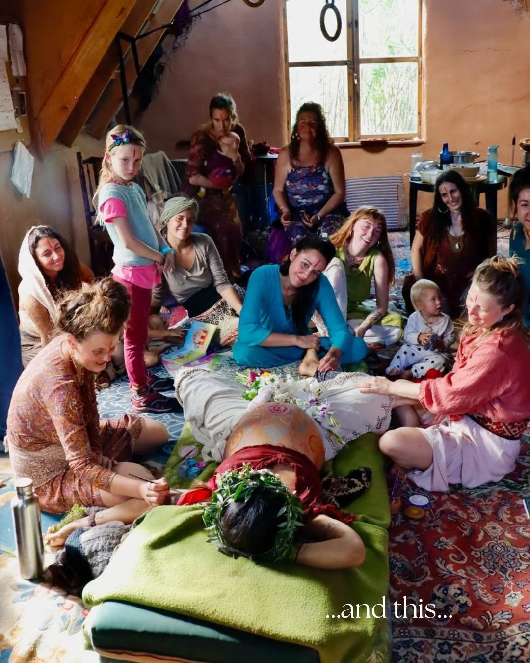 Group of women, children, and a girl wear traditional Indian clothing, participating in a cultural or ceremonial gathering in a cozy indoor setting. One woman lies on a bed with flowers and spiritual symbols, surrounded by others sitting and standing