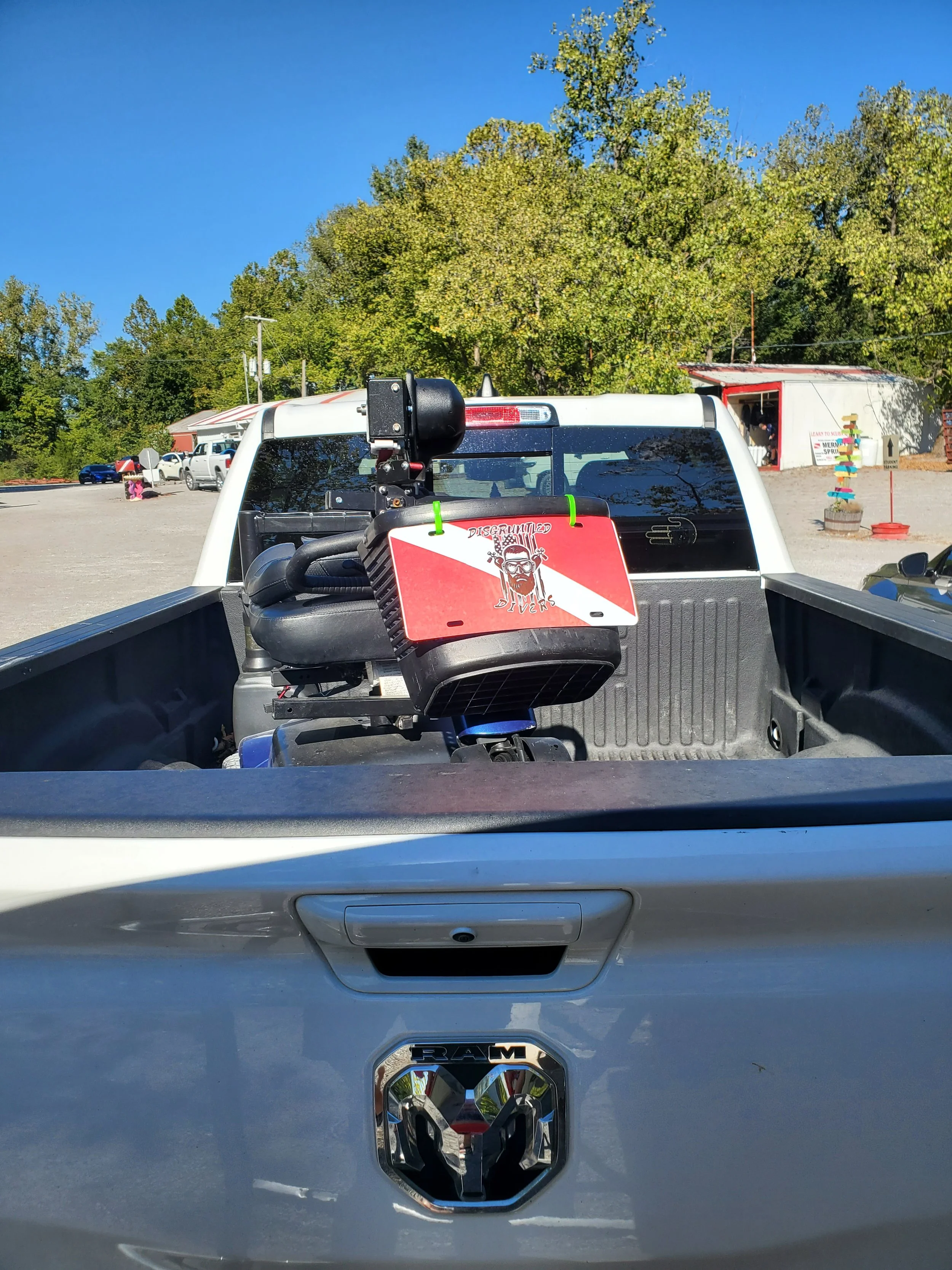 Back of a white truck with a RAM logo, carrying a small boat with a trolling motor attached. The trolling motor has a sign that reads 'Disqualified Diver' with a graphic of a diver wearing a mask and snorkel.