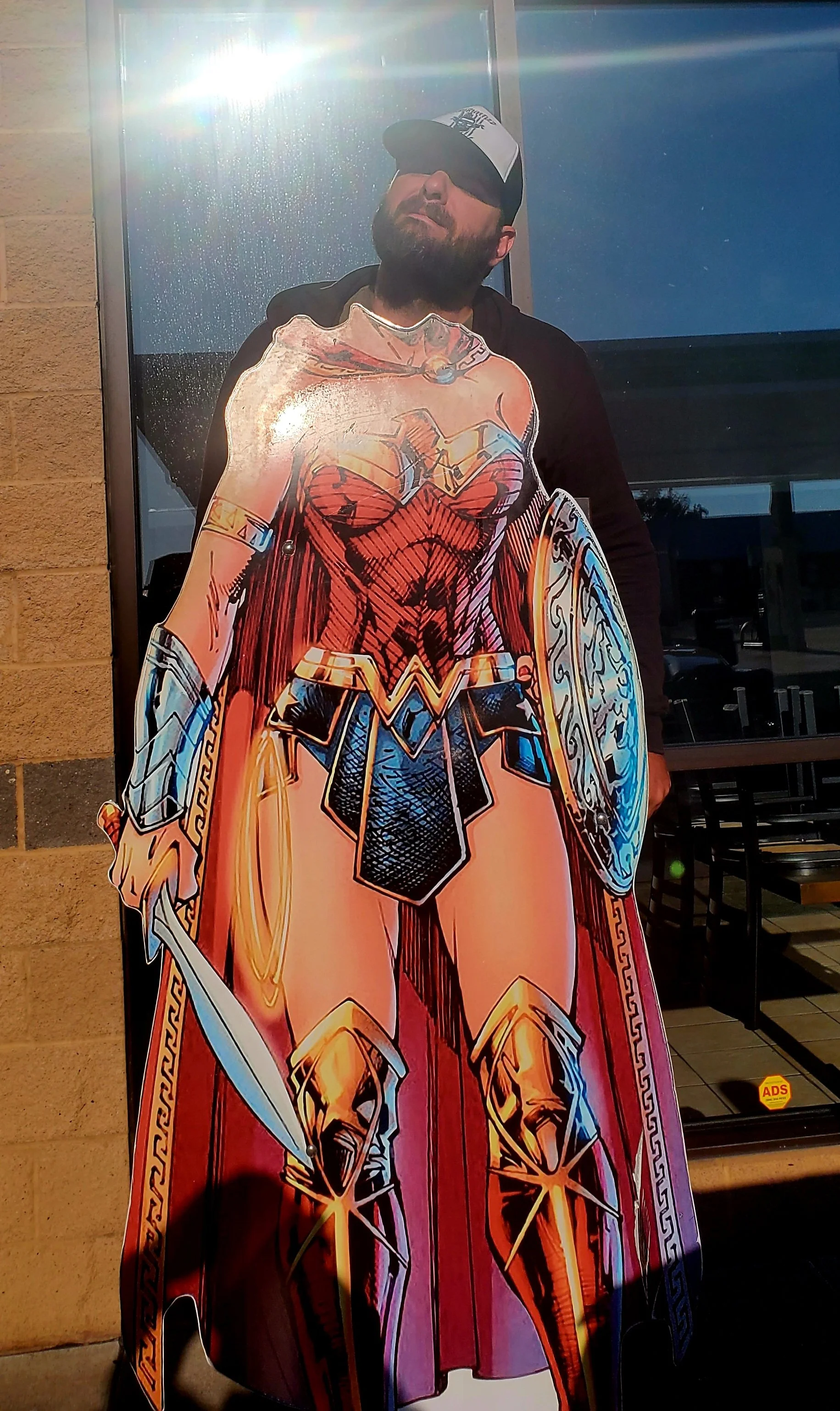 Man standing behind a Wonder Woman cutout display outside a building.