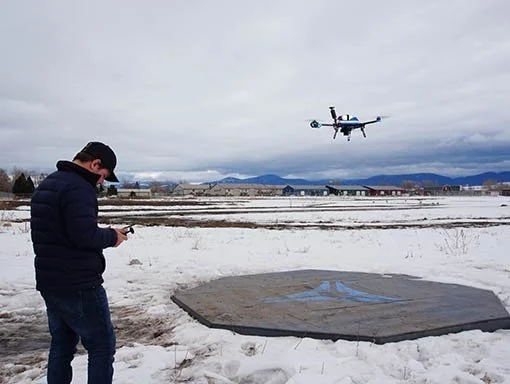 Drone pilot launching a drone over a snowy field to do an aerial survey for photogrammetry.