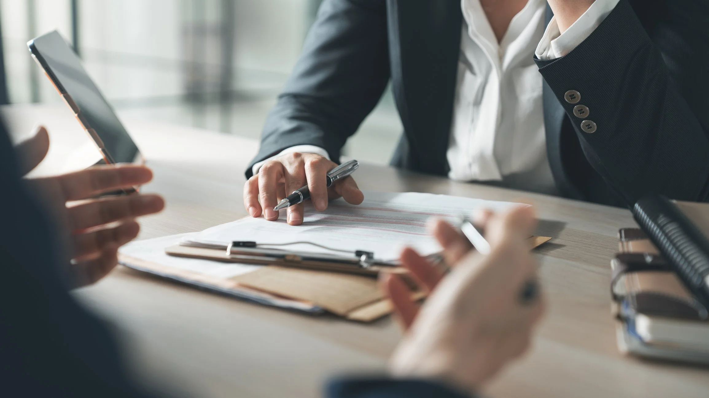 Business meeting with two people sitting at a table, one person is writing on a document while the other is holding a phone, in a professional office setting.