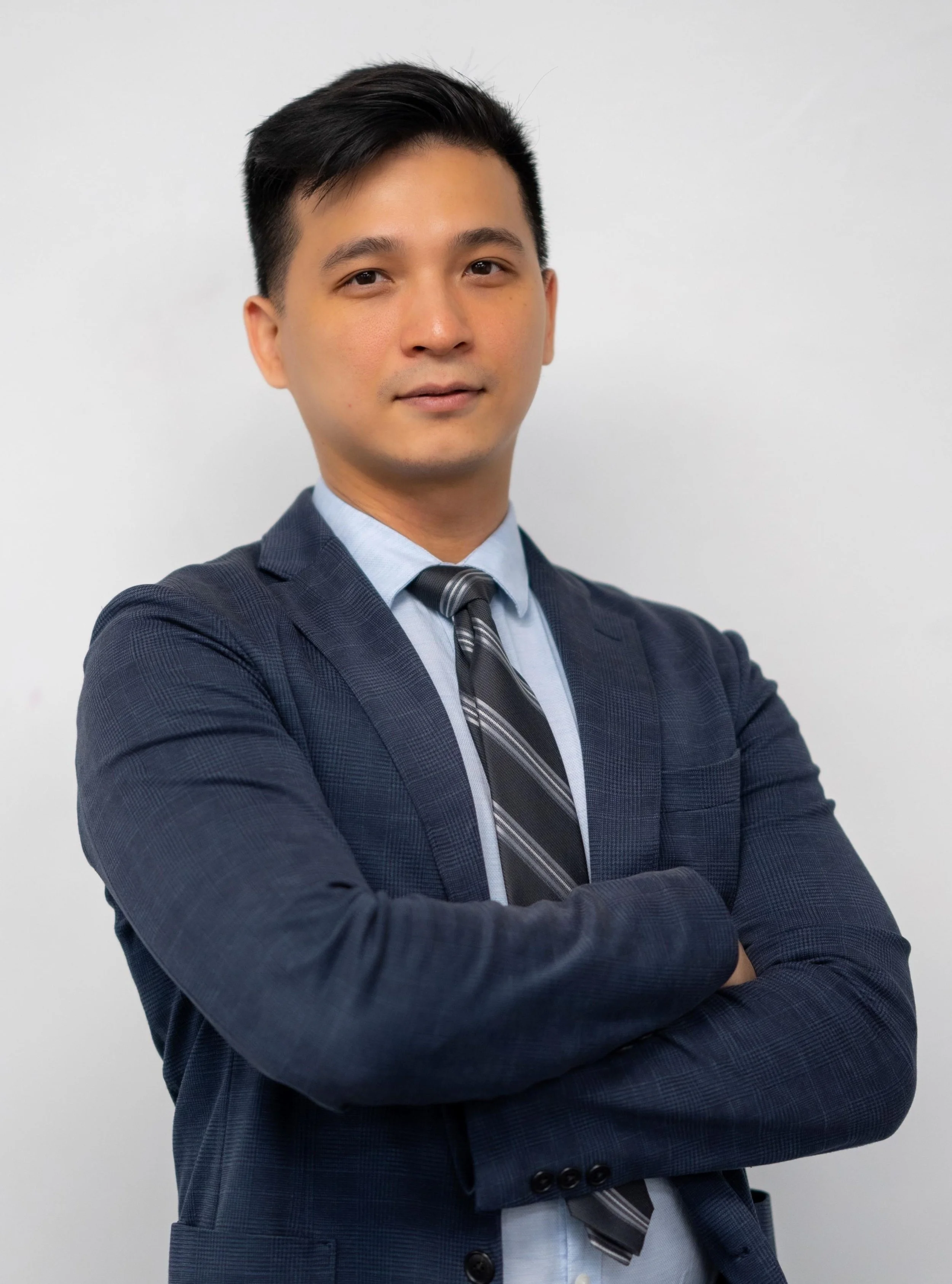 A man in a business suit with arms crossed against a white background.