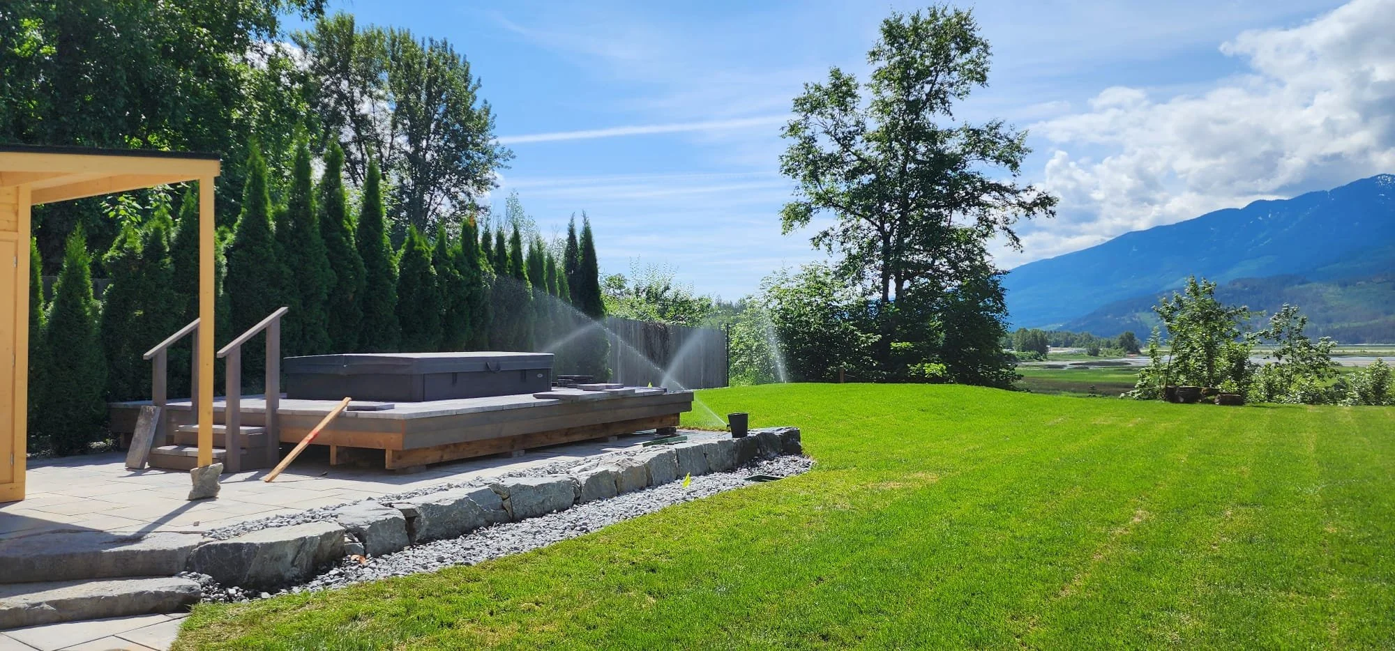 Backyard landscaping project featuring a retaining wall, natural lawn, and outdoor living space in Salmon Arm BC.
