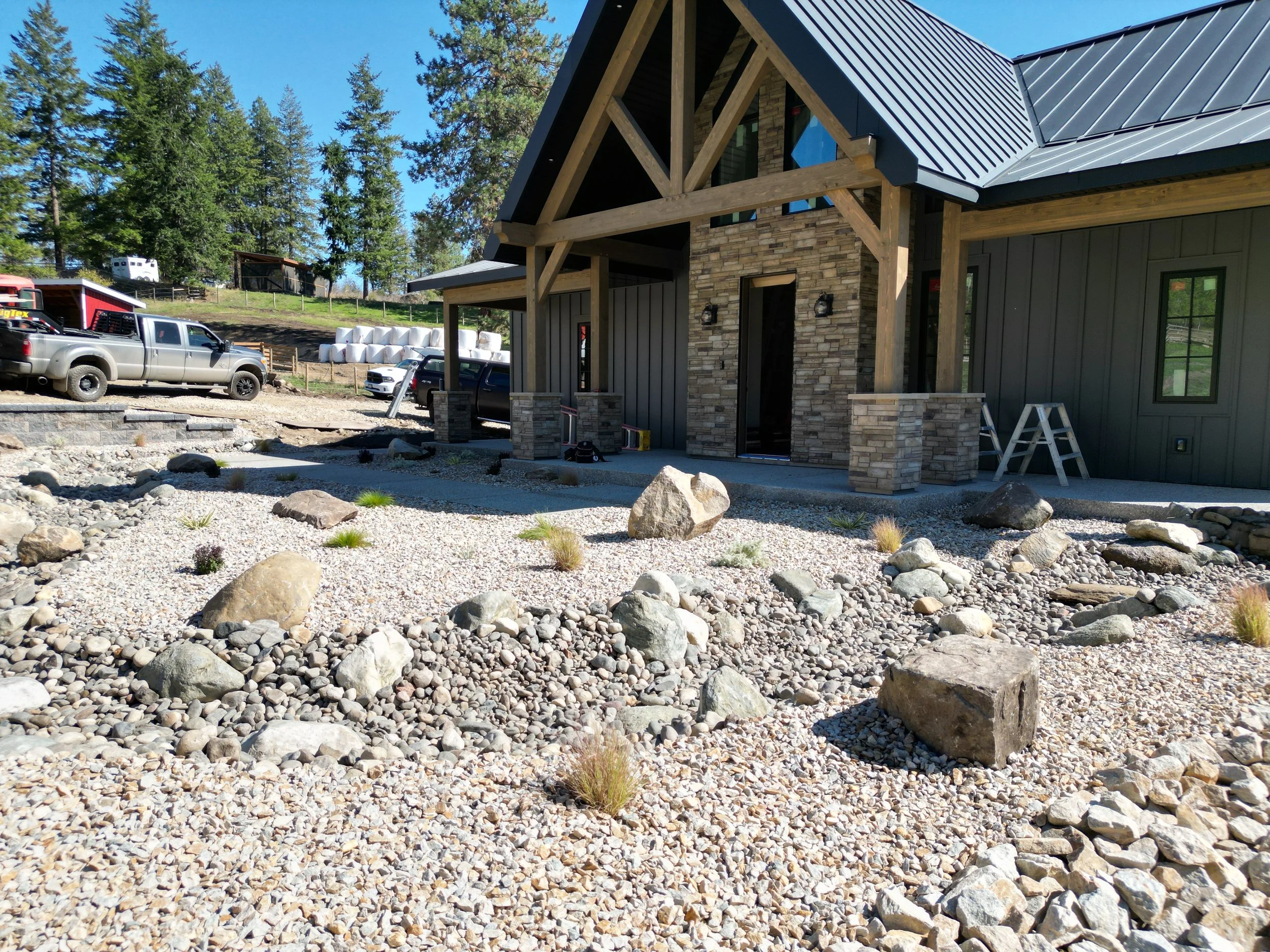 Low-maintenance residential landscaping featuring decorative rock, natural boulders, and clean landscape design around a custom home in the North Okanagan and Shuswap area.
