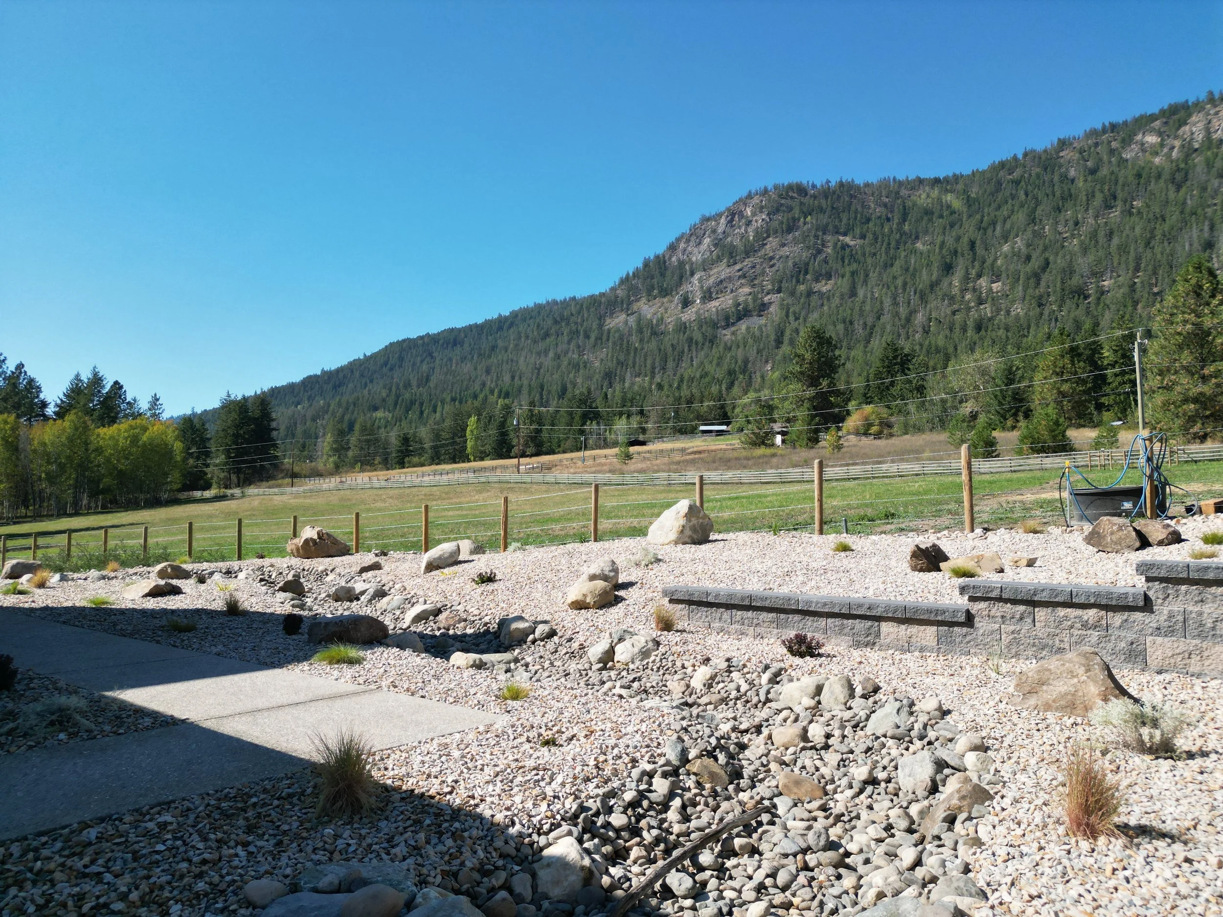 Dry creek and retaining wall installation in Armstrong, BC with decorative rock and natural landscape features for drainage, structure, and a clean finished look.