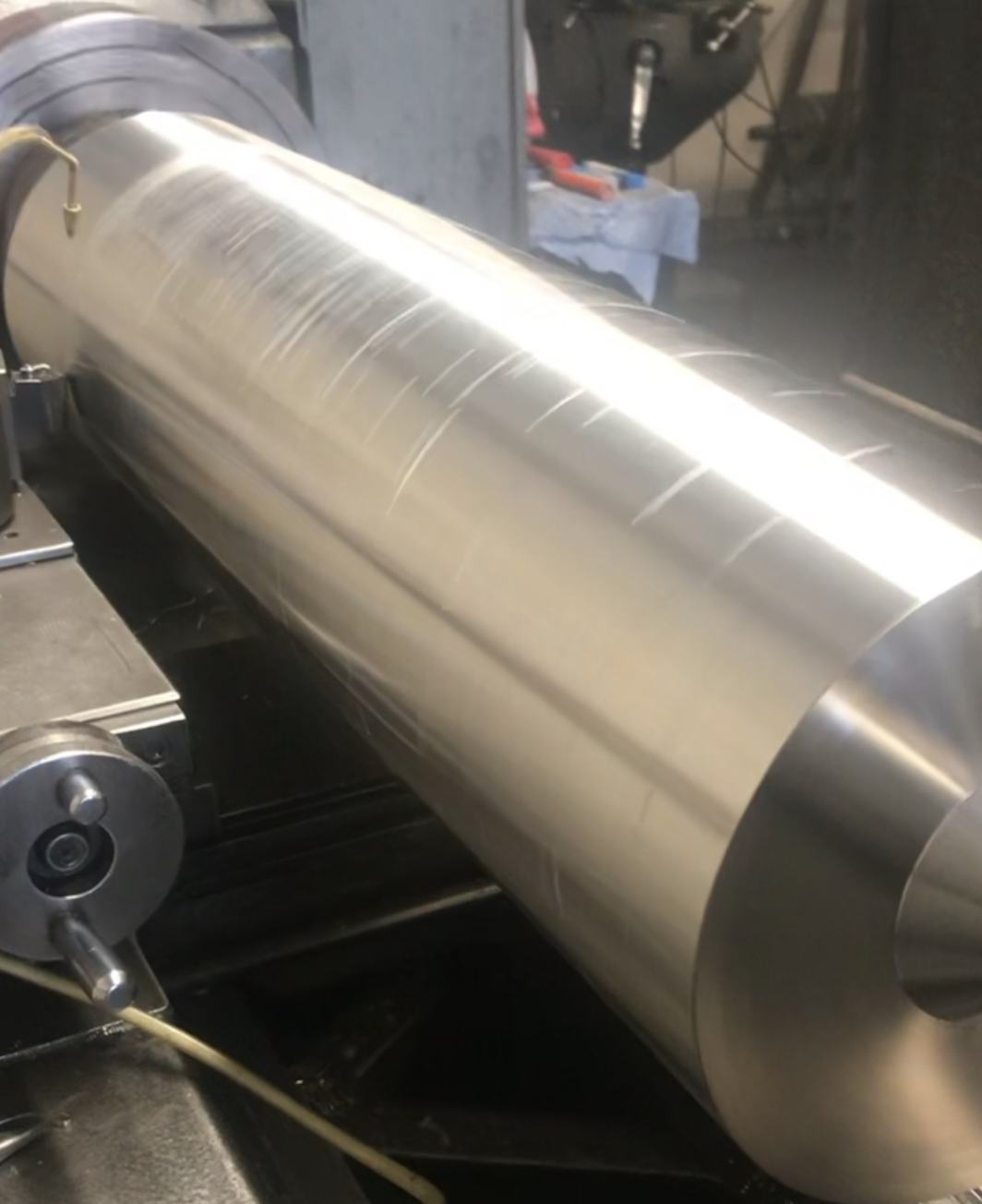 Close-up of a shiny, metallic, cylindrical industrial machine or roller in a manufacturing or workshop setting.