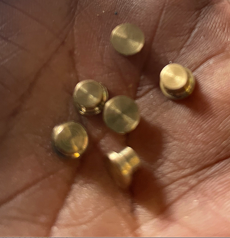 Close-up of six small, round, gold-colored metal beads resting on a person's palm.