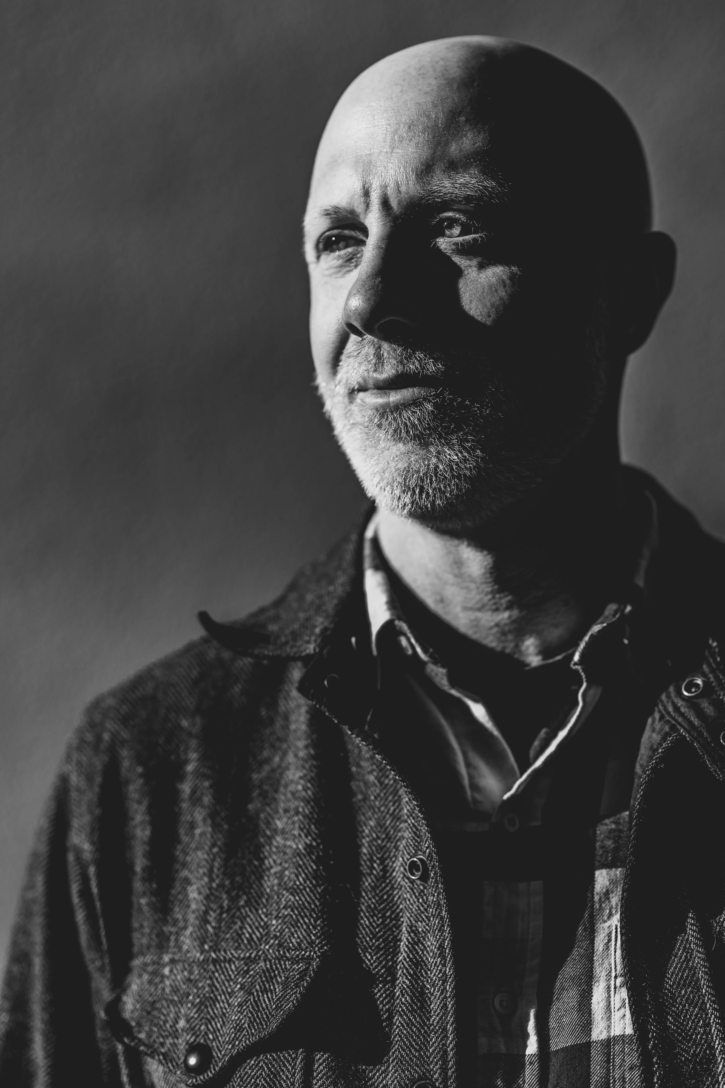 Black and white portrait Evan Hendrix a marriage coach in Leiden, Netherlands. He appears as a man with a bald head and gray beard, wearing a checkered shirt and jacket, looking to the side.
