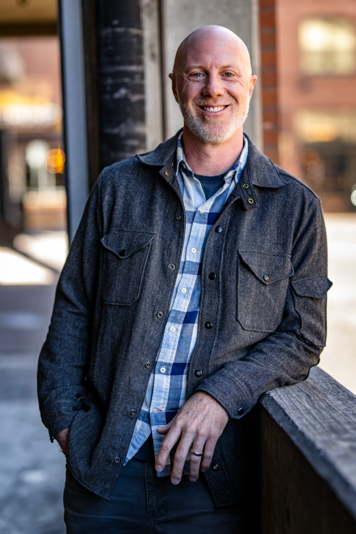 Evan Hendrix, marriage coach for men, smiling and leaning on a wooden rail in a herringbone jacket and blue plaid shirt