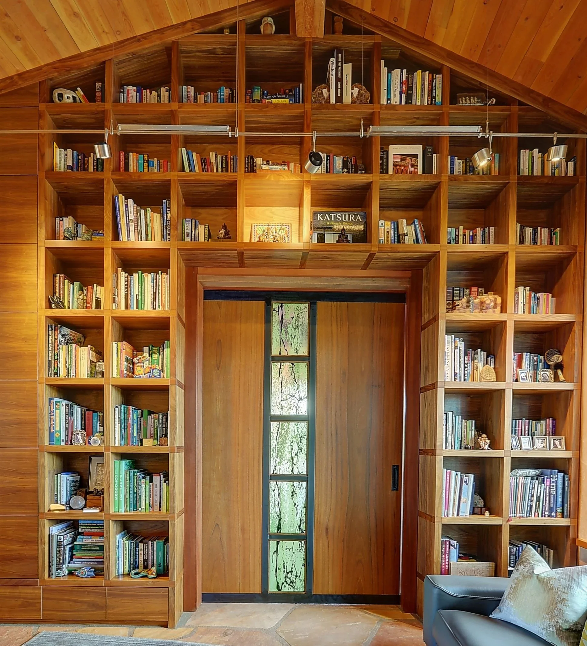 Wooden bookshelf with various books and decorative items, framing a custom wood door featuring a stained glass reveal.