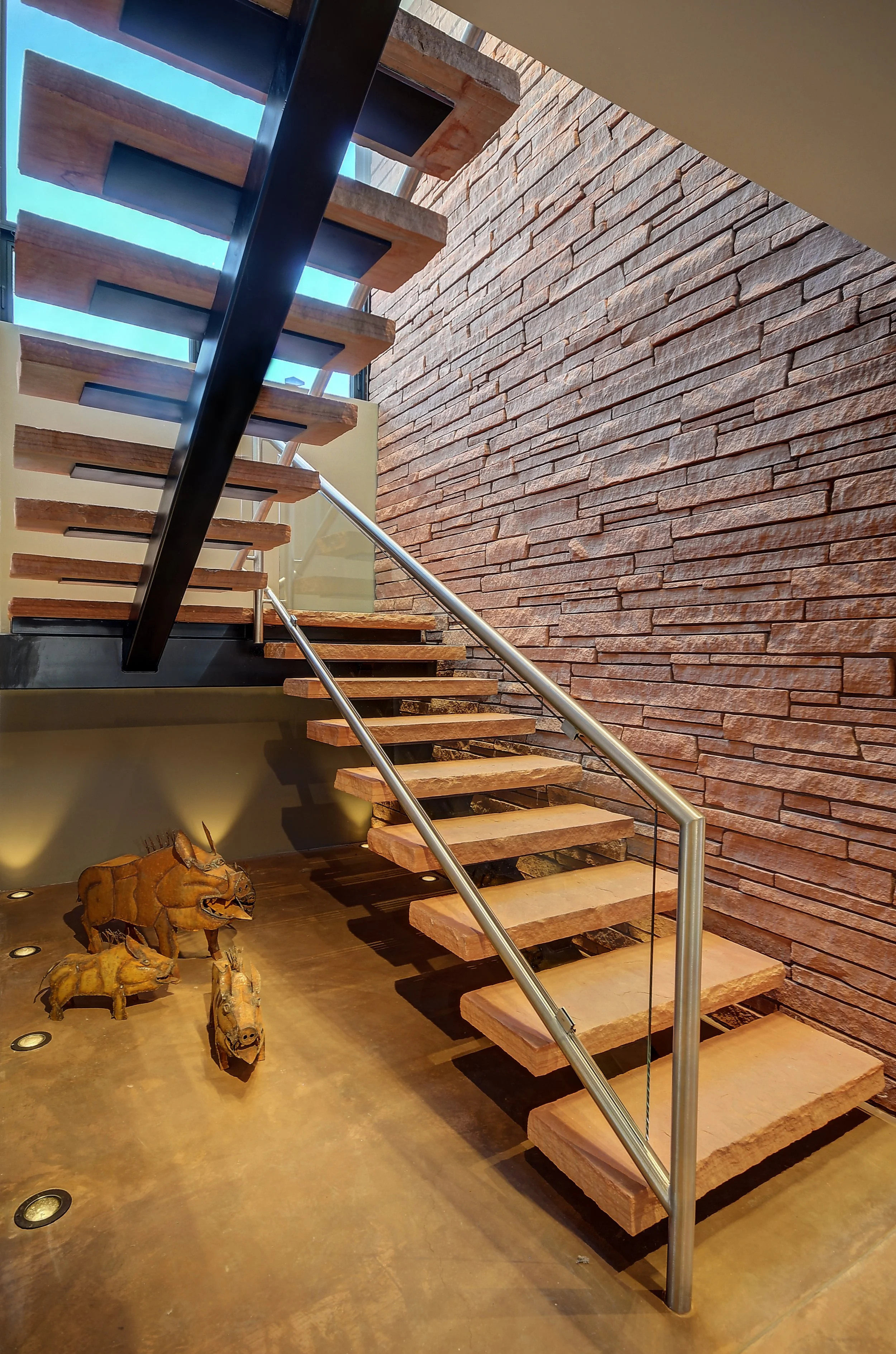 custom staircase with flagstone steps and a chrome round railing, with Javelina sculptures below.