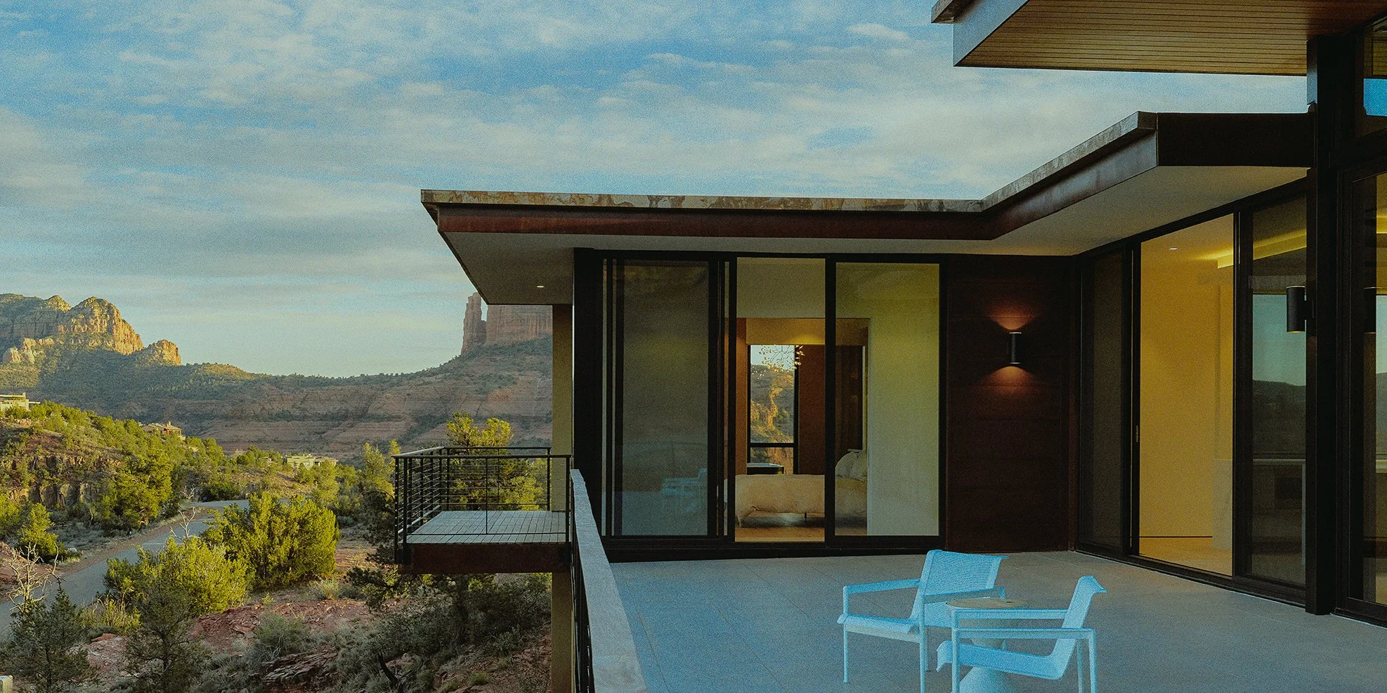 Modern house balcony with two white chairs overlooking a desert landscape with cliffs and a blue sky.