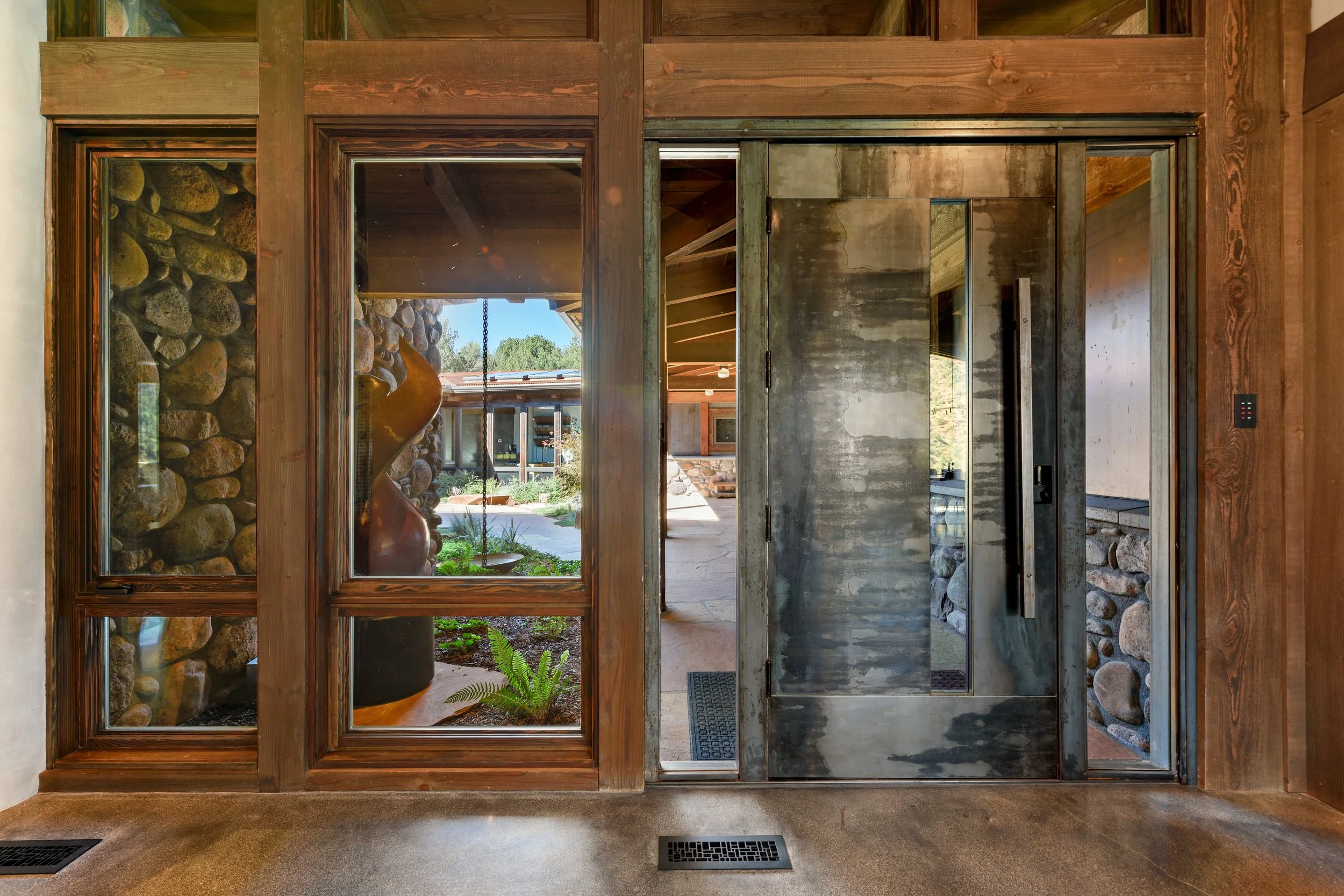 View showing a custom fabricated steel door with an asymmetric glass opening, and two side lights, surrounded by dark wood trim.
