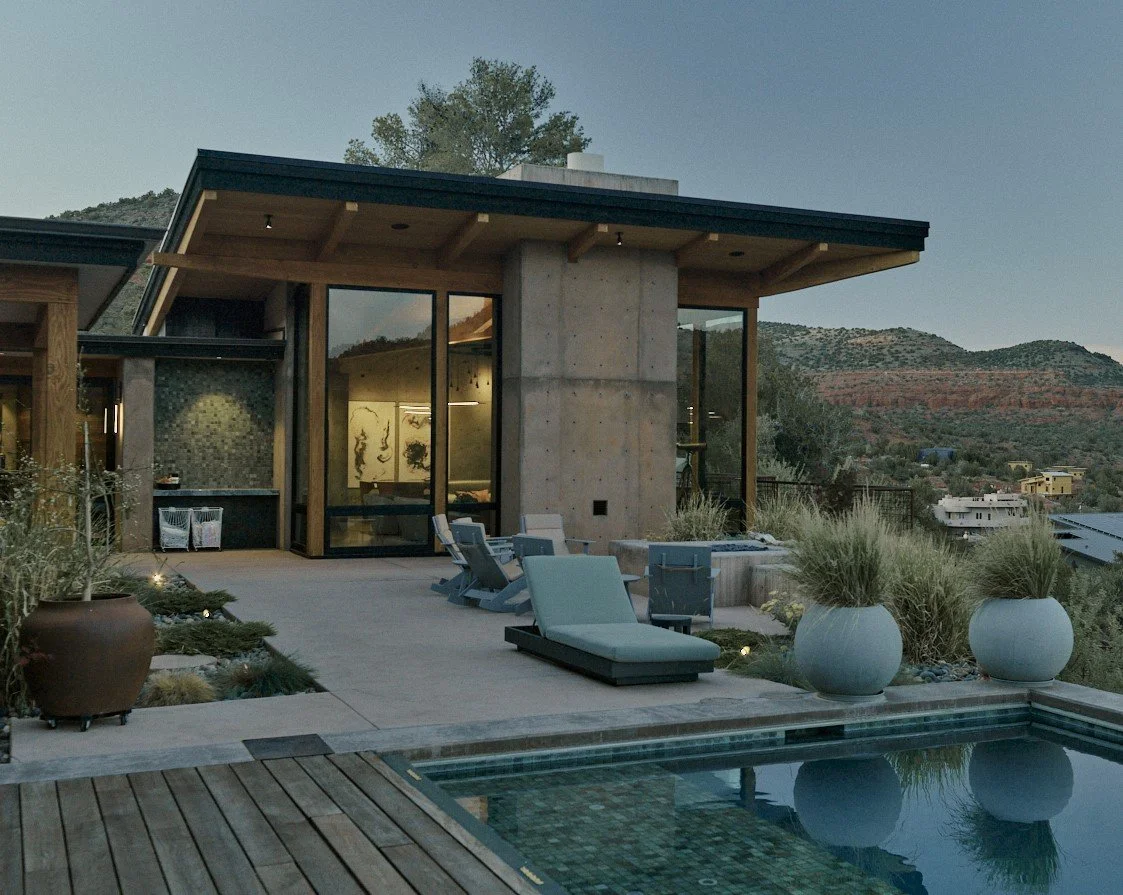 Modern house with outdoor patio, lounge chair, potted plants, and swimming pool, set against a hilly landscape during dusk.