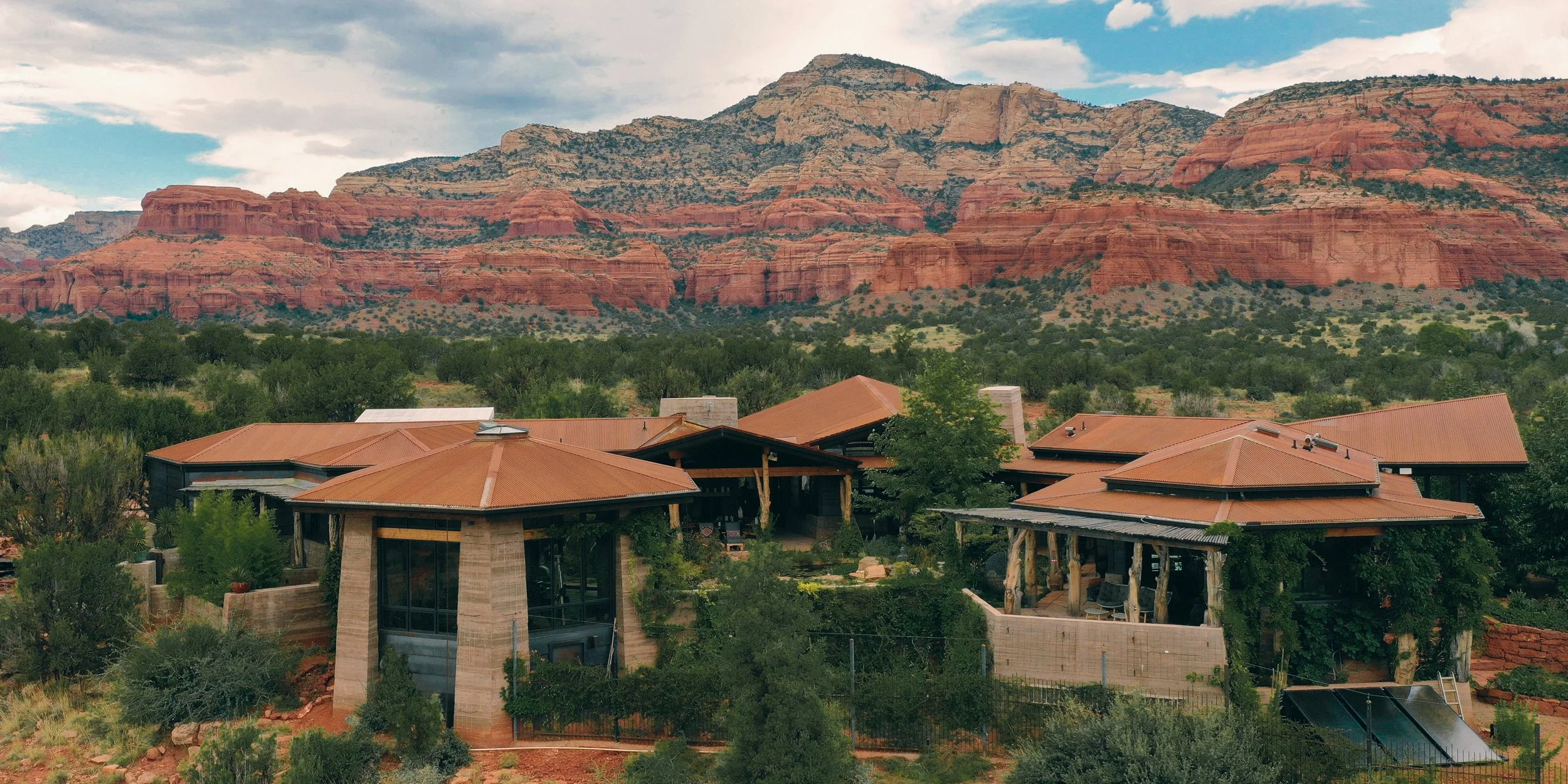 Residential houses with red-tile roofs surrounded by desert vegetation, with red rock formations and mountains in the background.