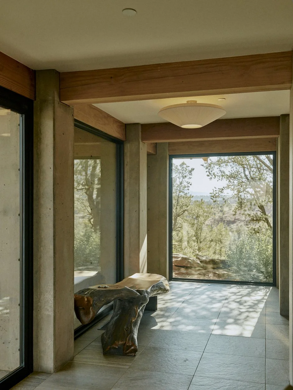 A modern interior space with large windows, concrete pillars, a wooden ceiling beam, and a custom wooden bench near the window, overlooking the landscape of Sedona, Arizona.