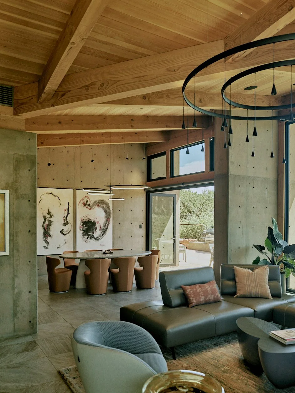 Modern living room with wooden ceiling, concrete walls, glass doors, contemporary furniture, wall art, and a view outside.