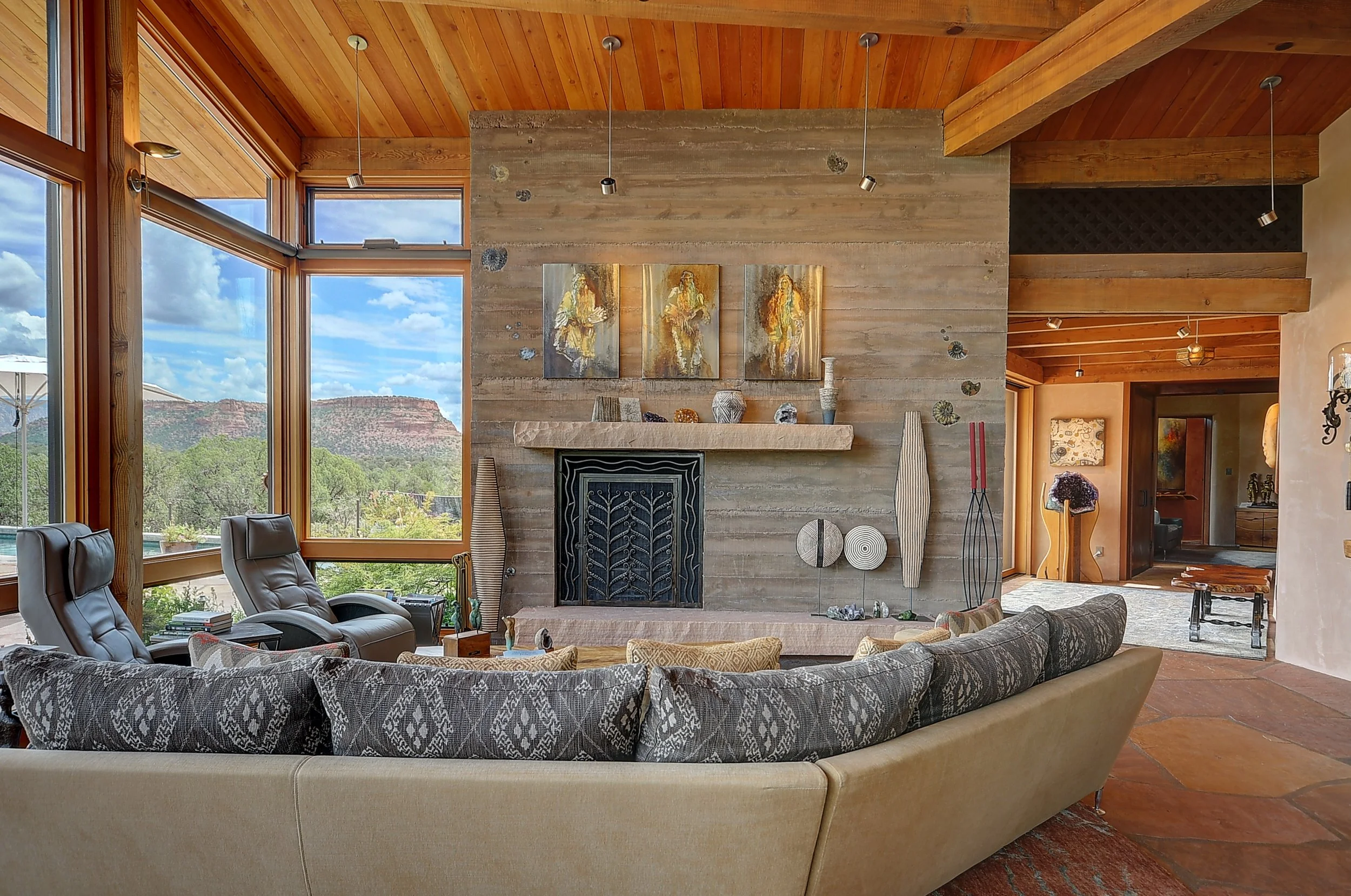 Living room with large windows, wooden ceiling, stone fireplace, and modern decor including art pieces, vases, and chairs, overlooking the landscape of Sedona, Arizona.