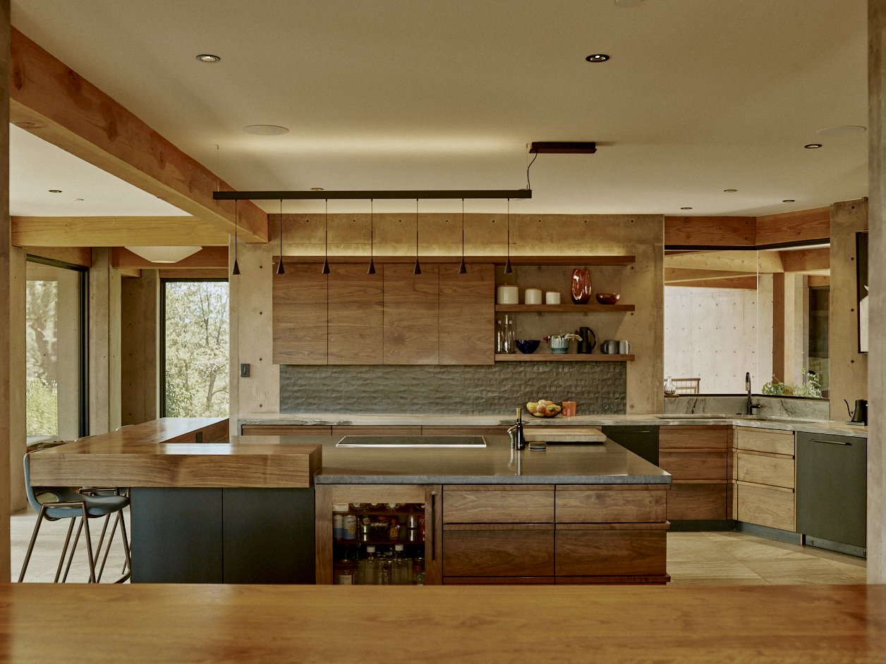 Modern kitchen with wooden cabinets, gray countertops, open shelving with dishes, and a central island with barstools.