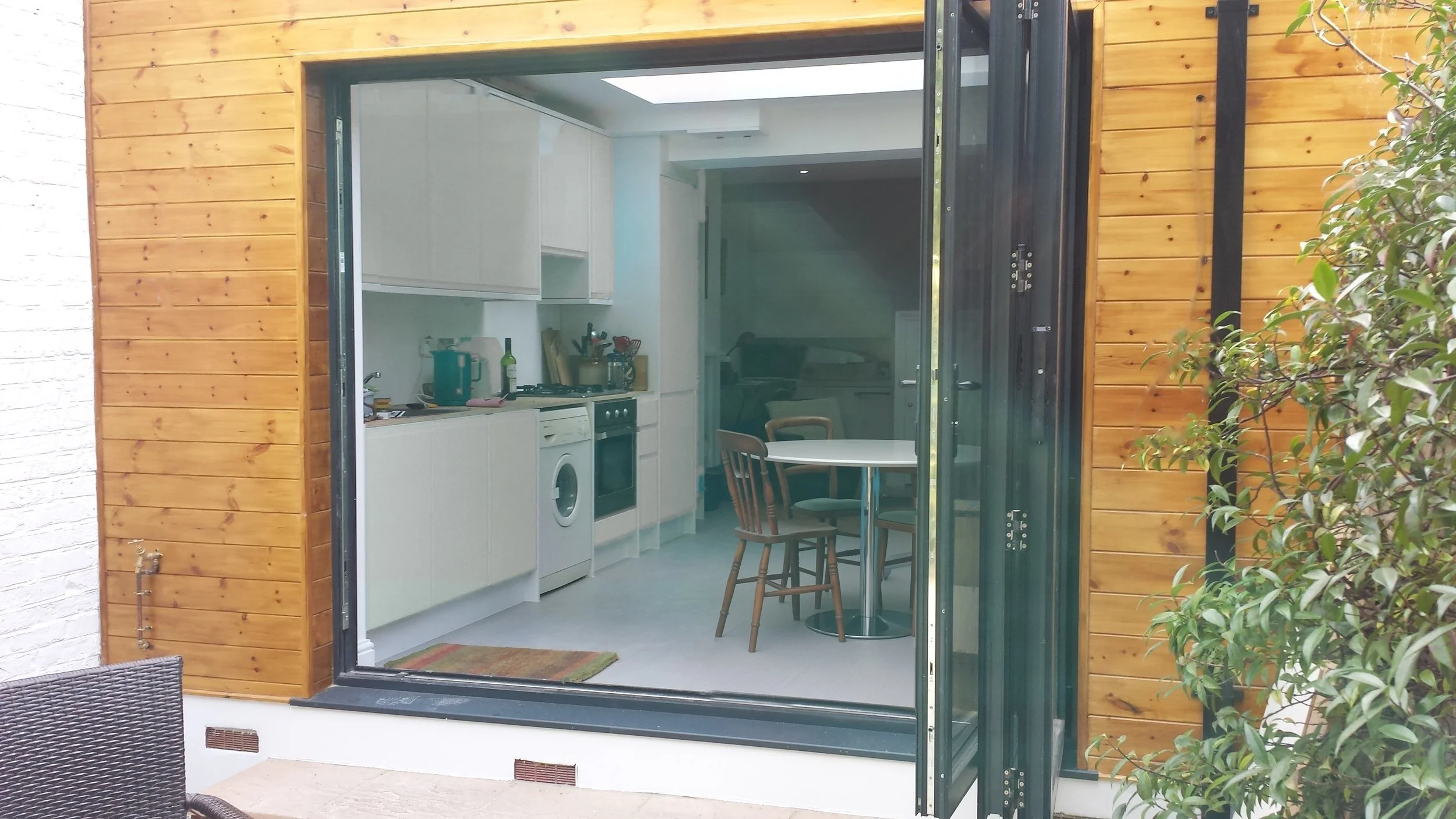 Bifold doors folded open onto the garden, showing the kitchen-diner inside at a rear kitchen extension on Short Road, Chiswick, W4 by Robin Services.