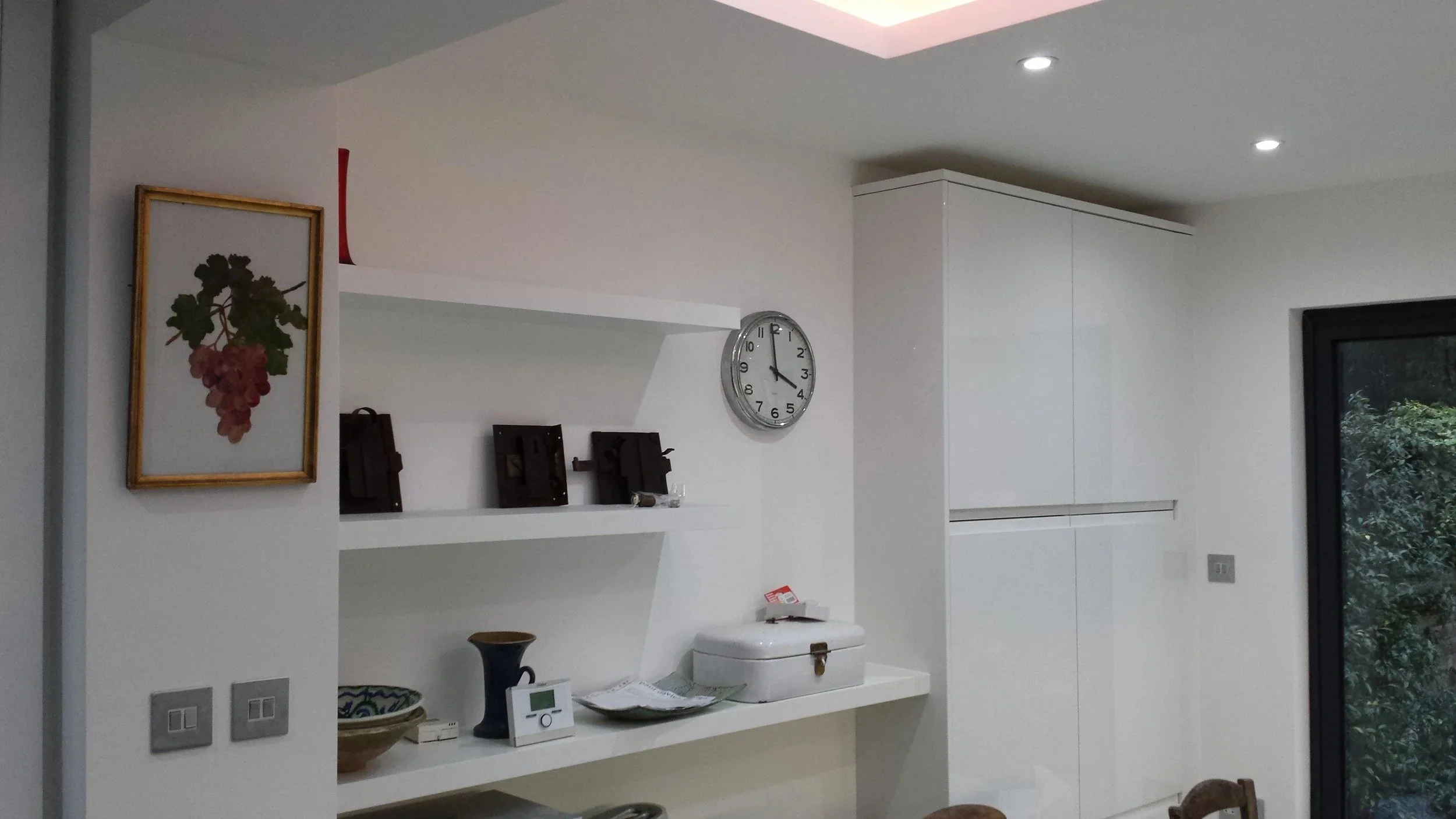 White floating shelves and tall handleless units on the kitchen wall at a rear kitchen extension on Short Road, Chiswick, W4 by Robin Services.