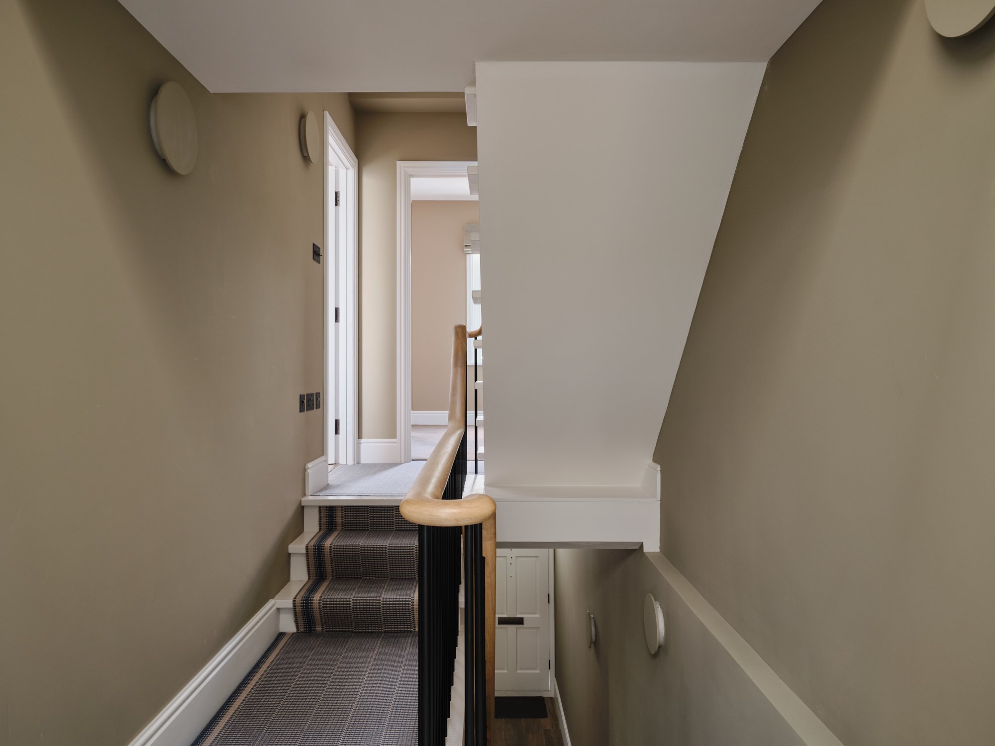 Stairwell landing with wooden handrail and beige walls at a house renovation on Priory Road, Chiswick, W4 by Robin Services.