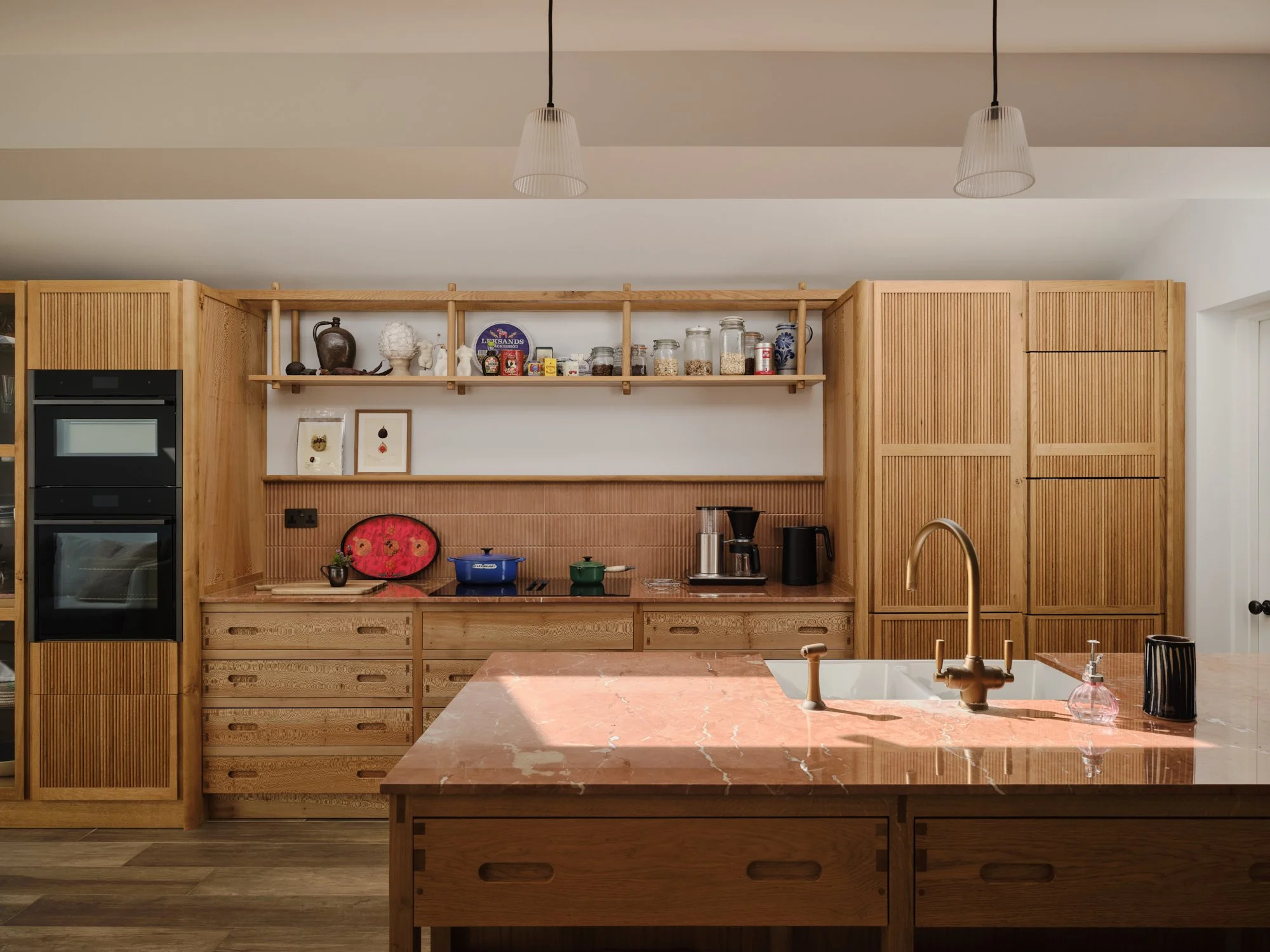 Bright modern kitchen with light wood cabinetry, a reddish marble island, and brass accents