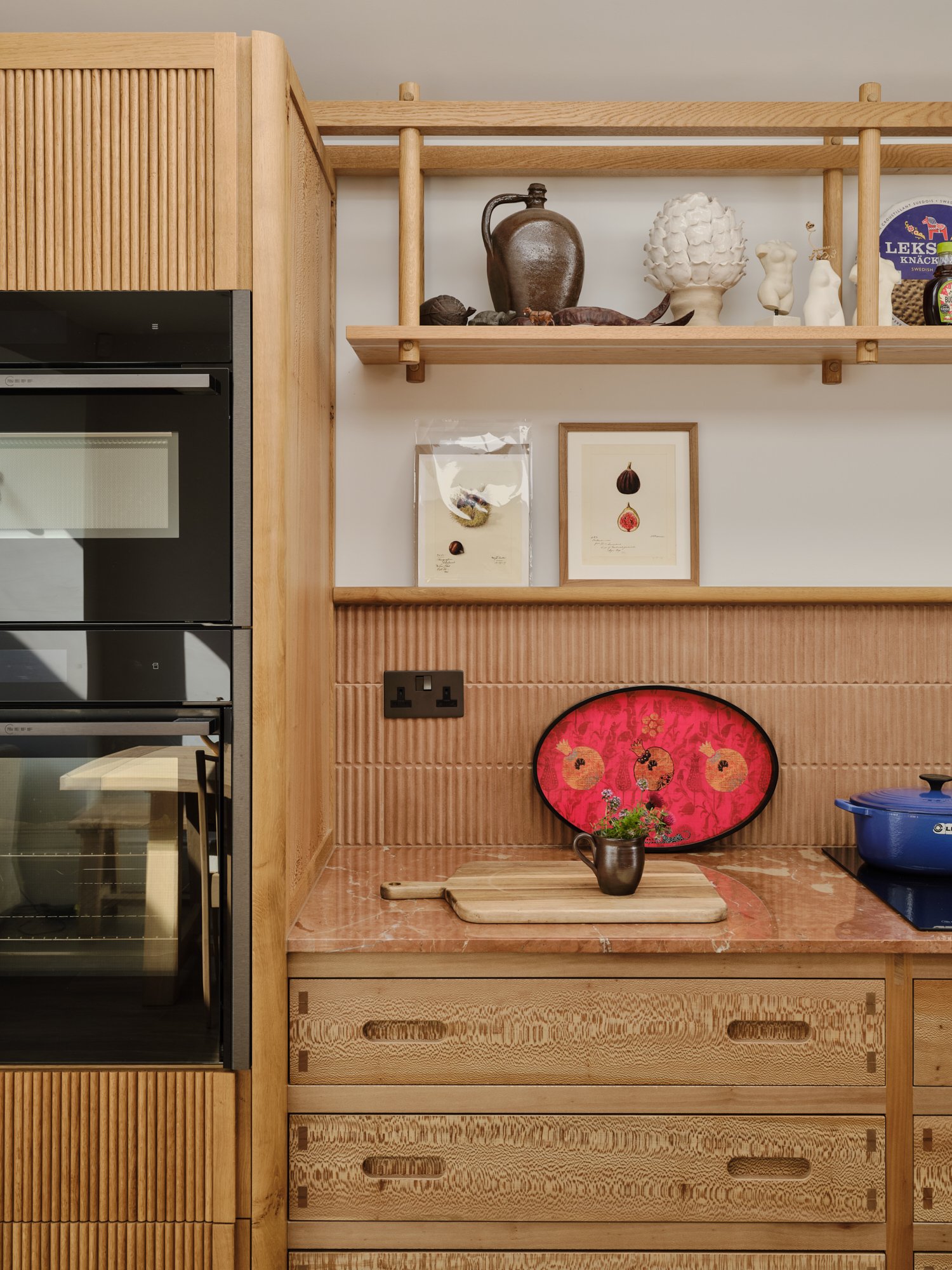 Black oven beside oak shelving with red kitchen accessories at a house renovation on Priory Road, Chiswick, W4 by Robin Services.