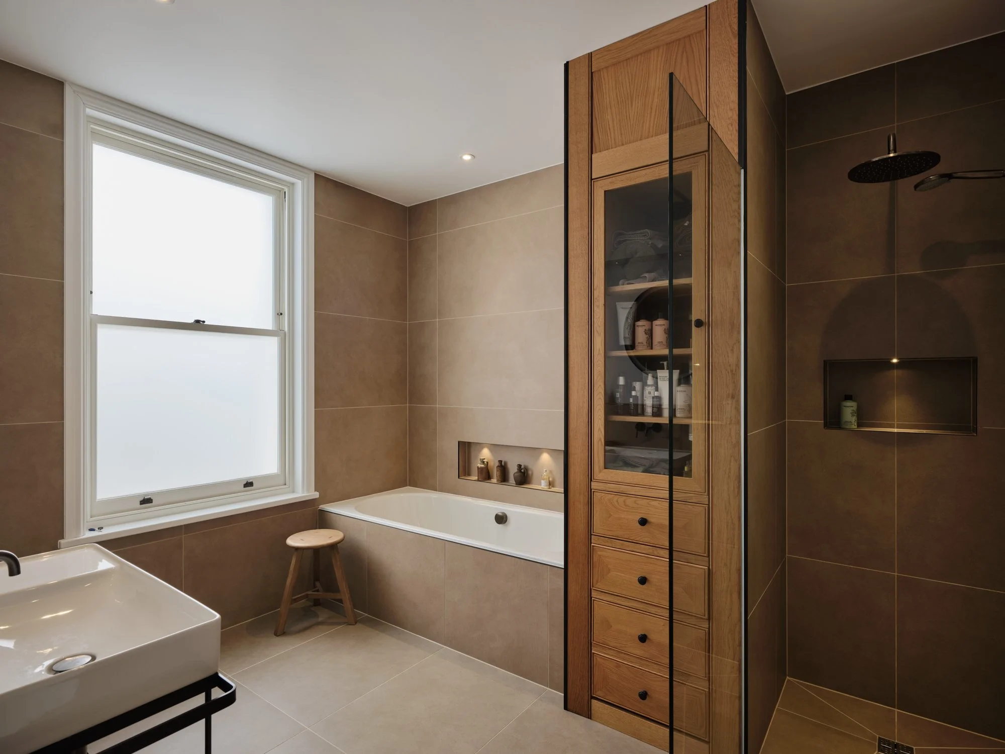 Elegant contemporary bathroom featuring a walk-in rainfall shower, built-in bathtub, bespoke oak cabinetry, and warm neutral finishes.