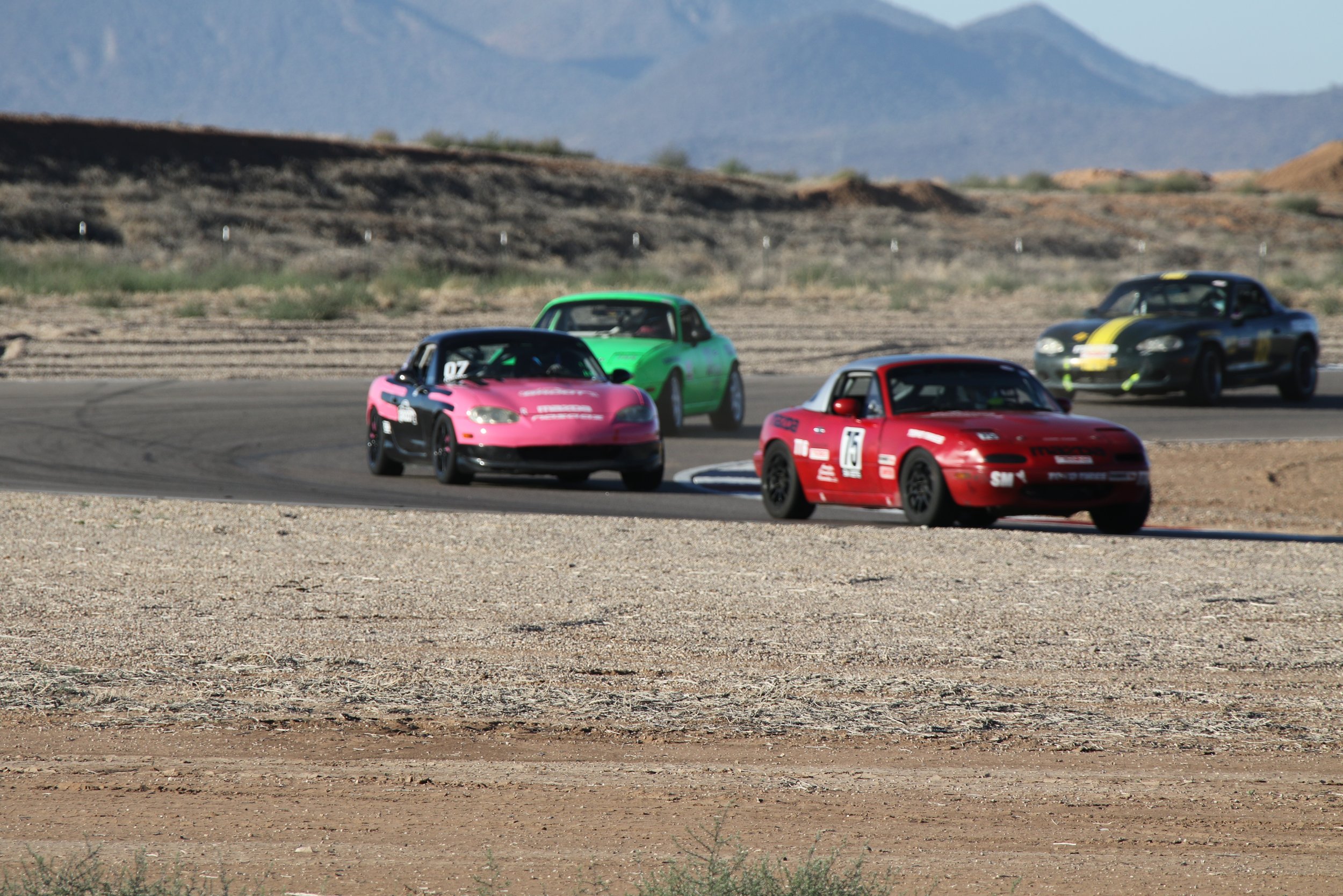 Four race cars on a desert race track with mountains in the background.