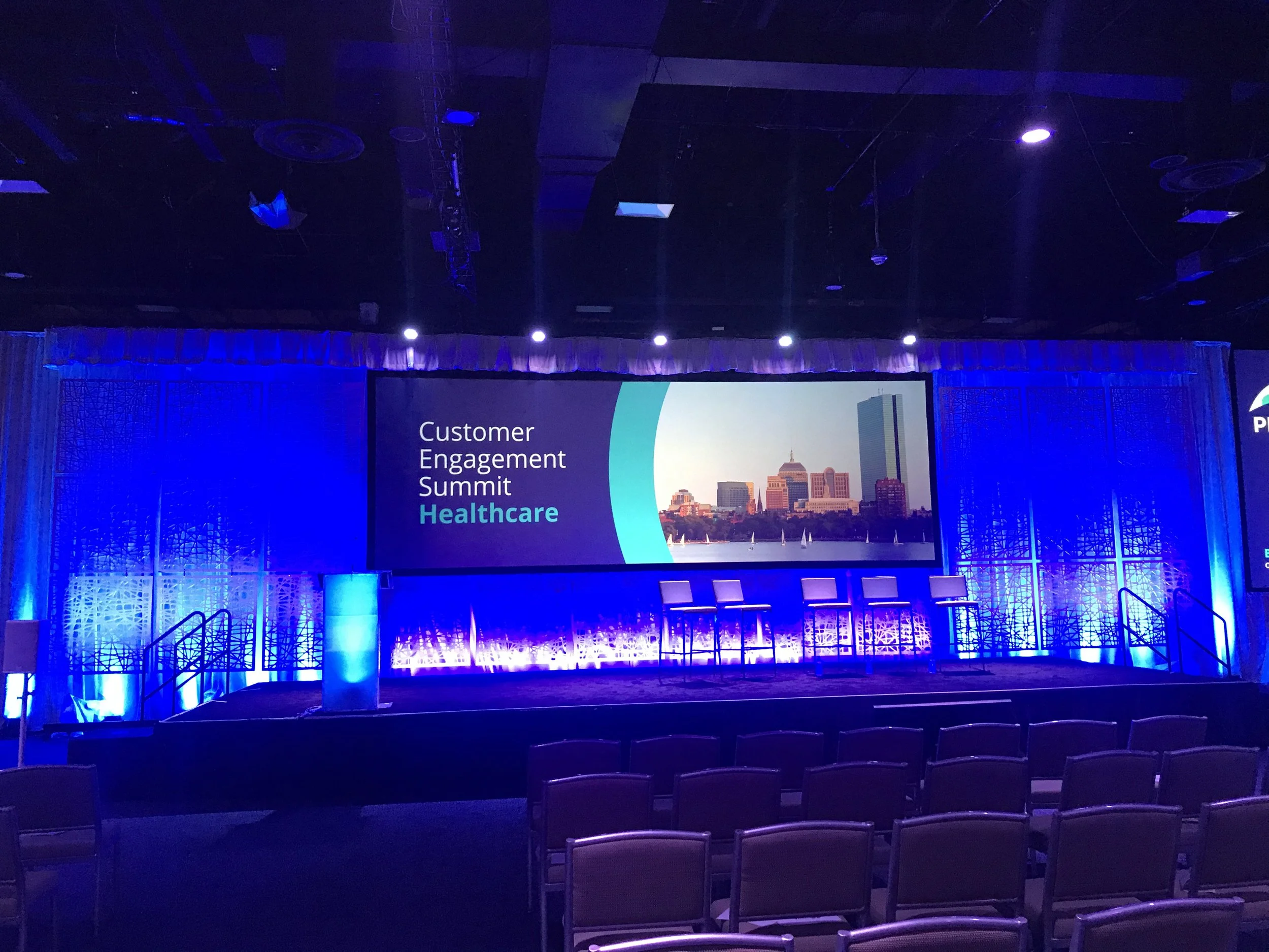 Stage set for the Customer Engagement Summit Healthcare, with a large screen and purple lighting.