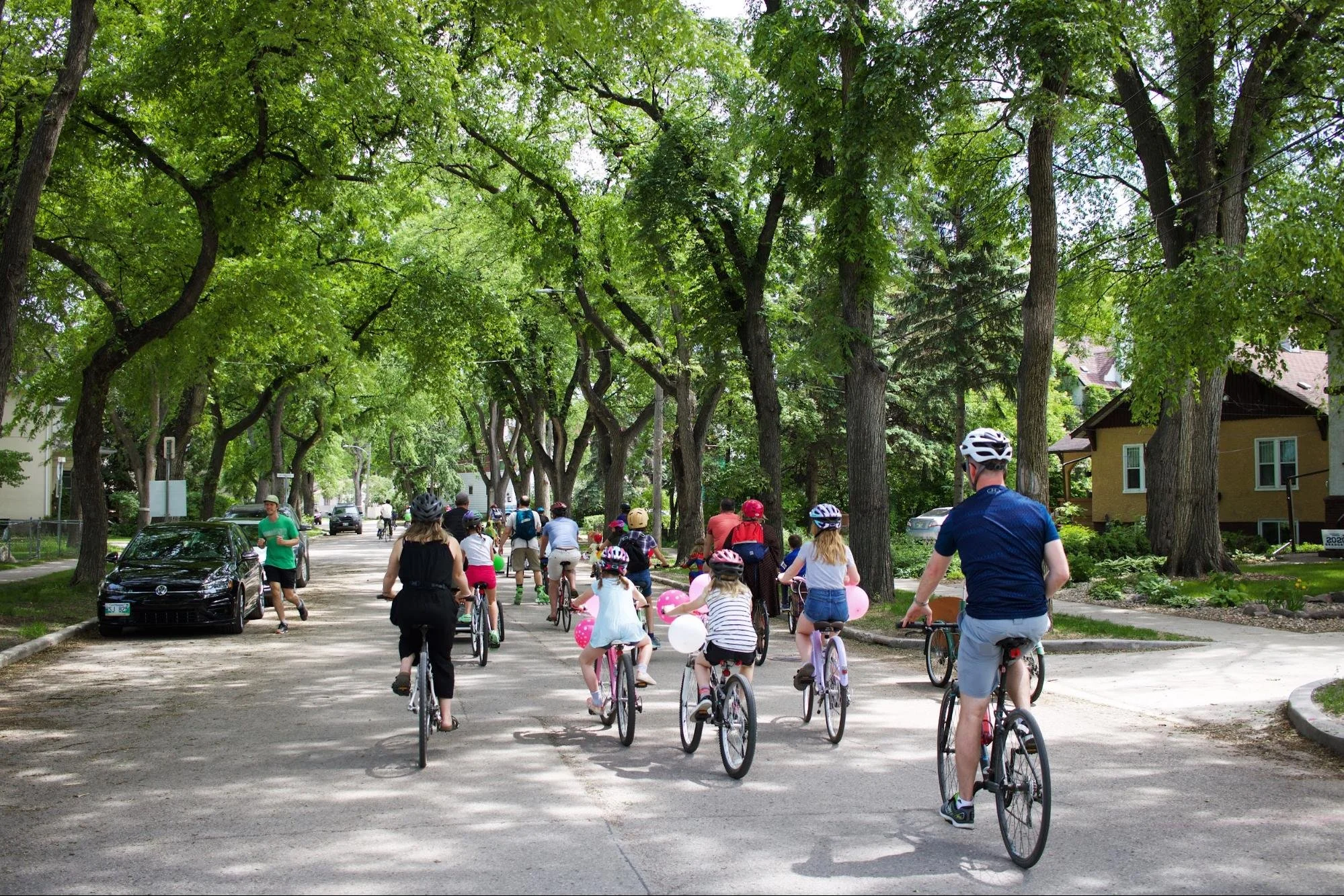 A group of all ages enjoying a bike ride on a tree-lined street