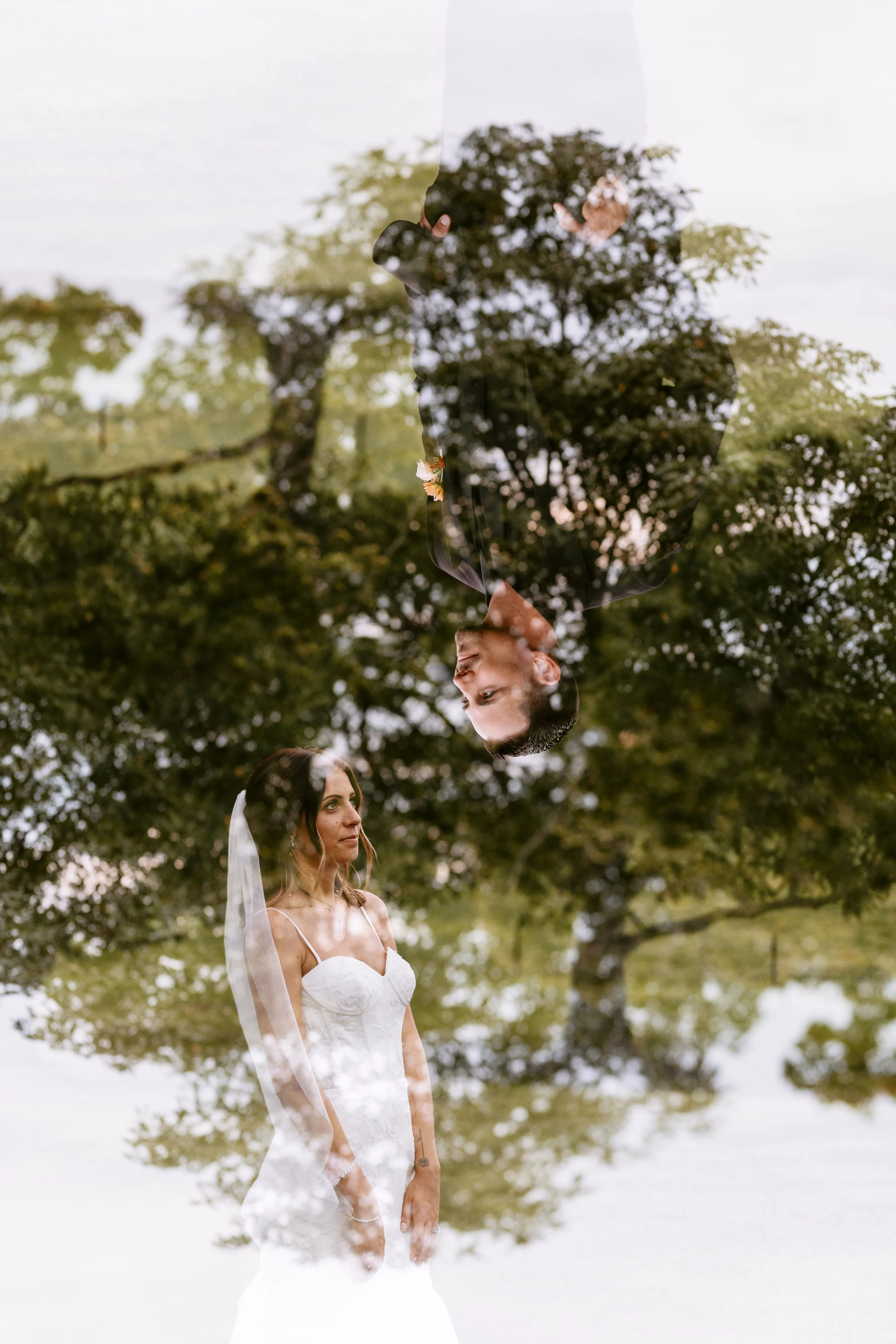 A double exposure photo of a bride and groom, with the groom's reflection on a glass, and trees in the background.