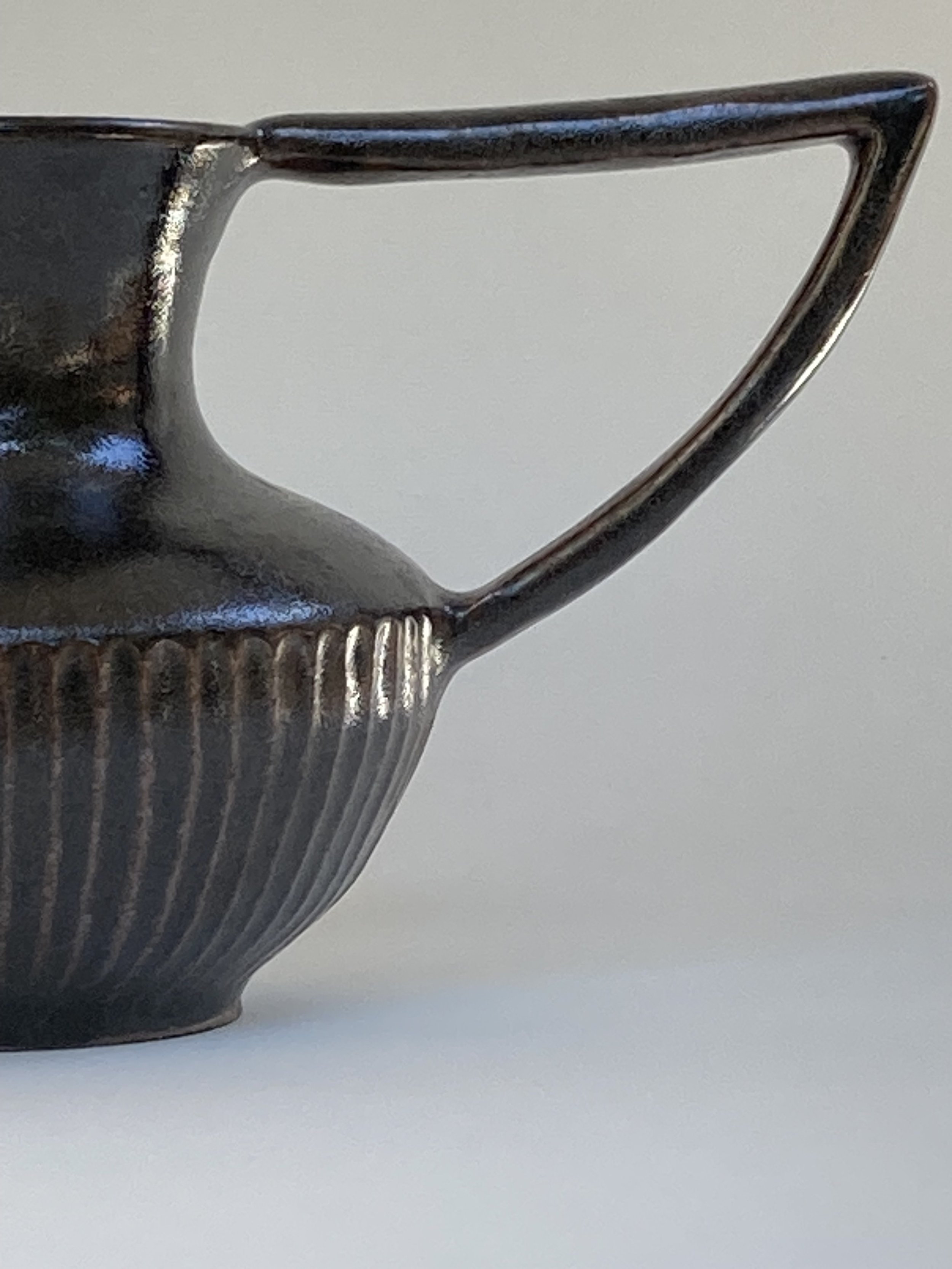 Close-up photo of a black ceramic cup with a textured, ribbed bottom and a large, curved handle, set against a plain white background.