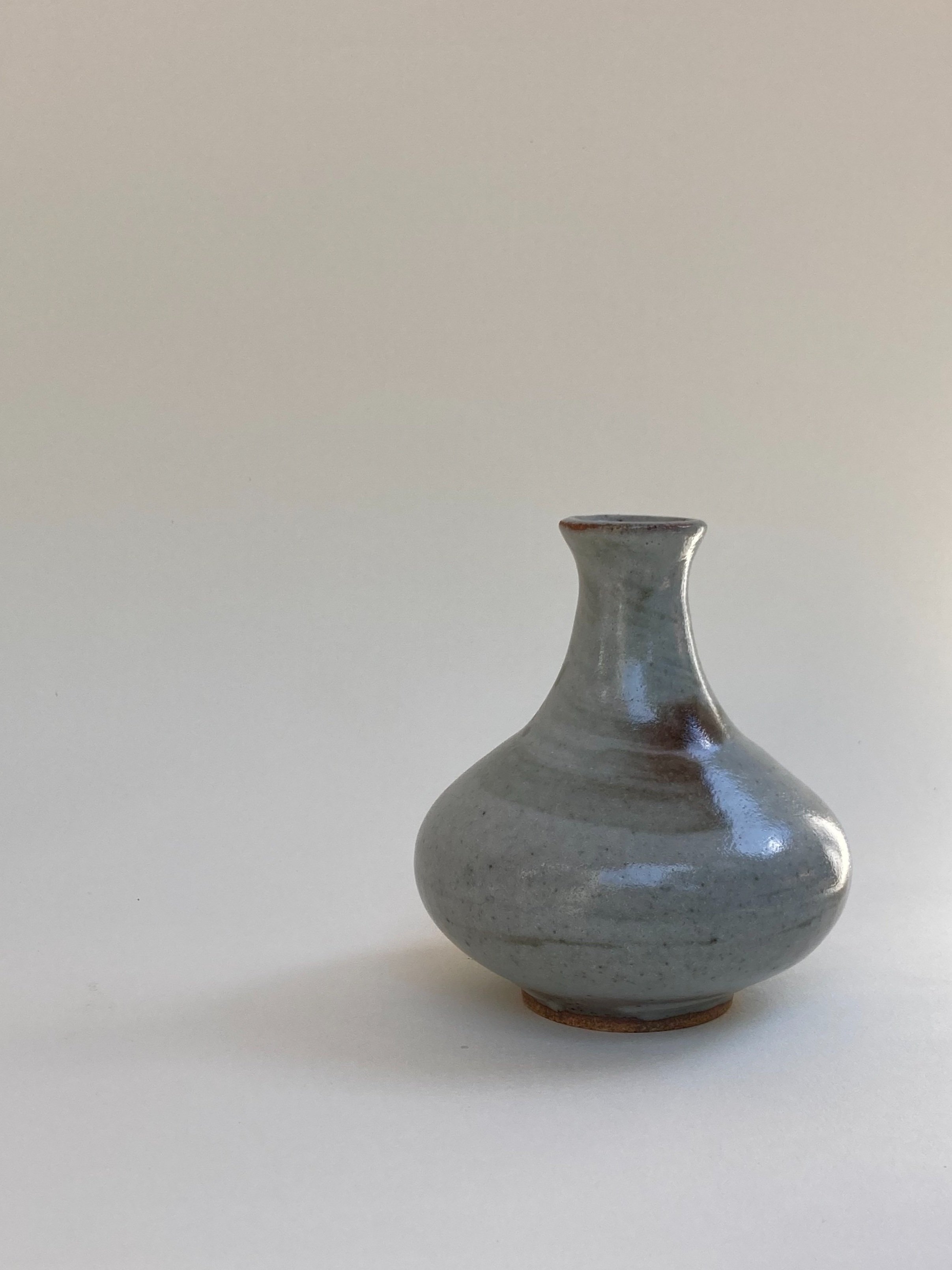 Small gray ceramic vase with a narrow neck and rounded body, placed on a white surface against a plain light background.